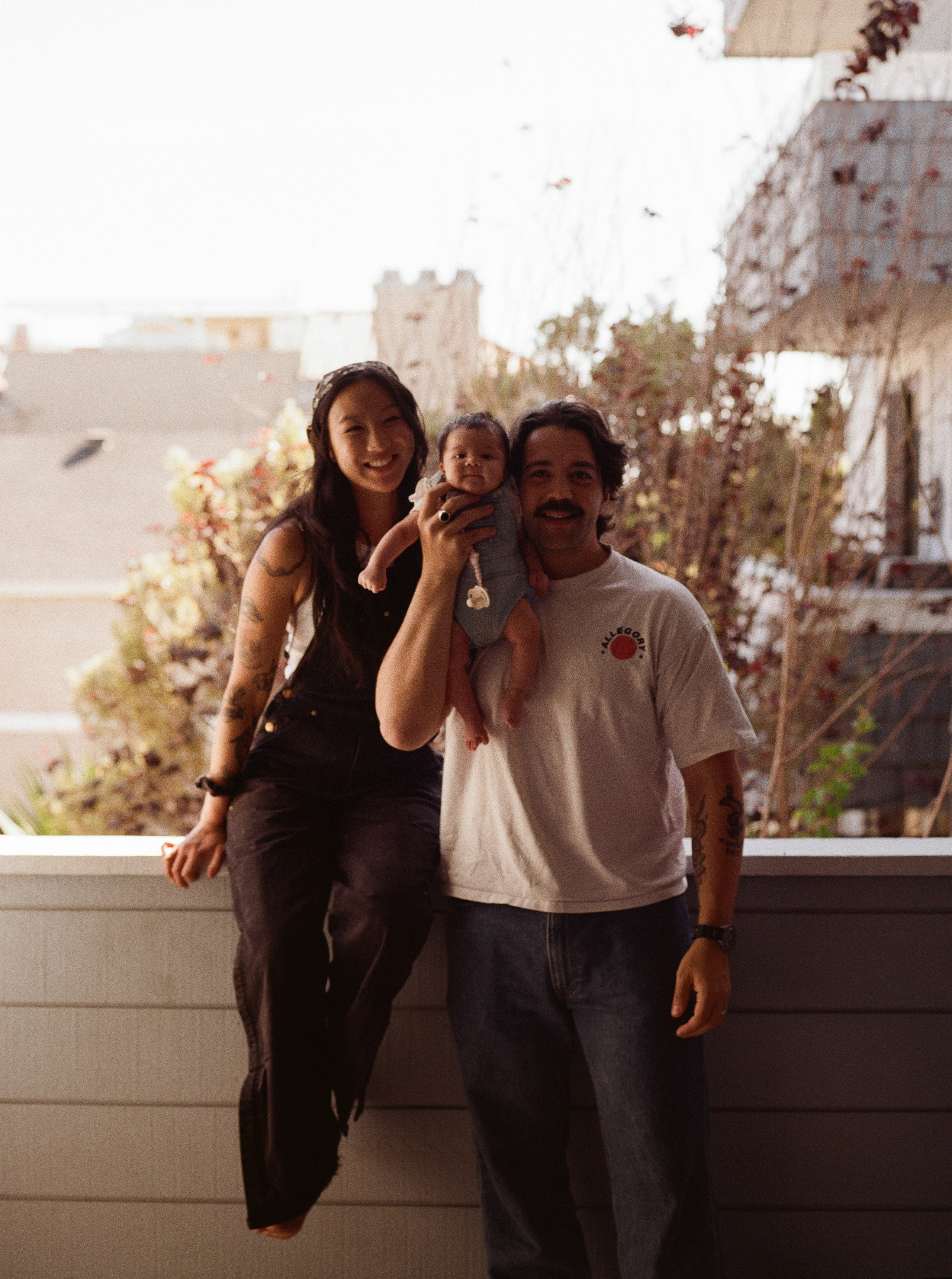 Mum, dad and baby girl on their balcony looking in the camera and smiling