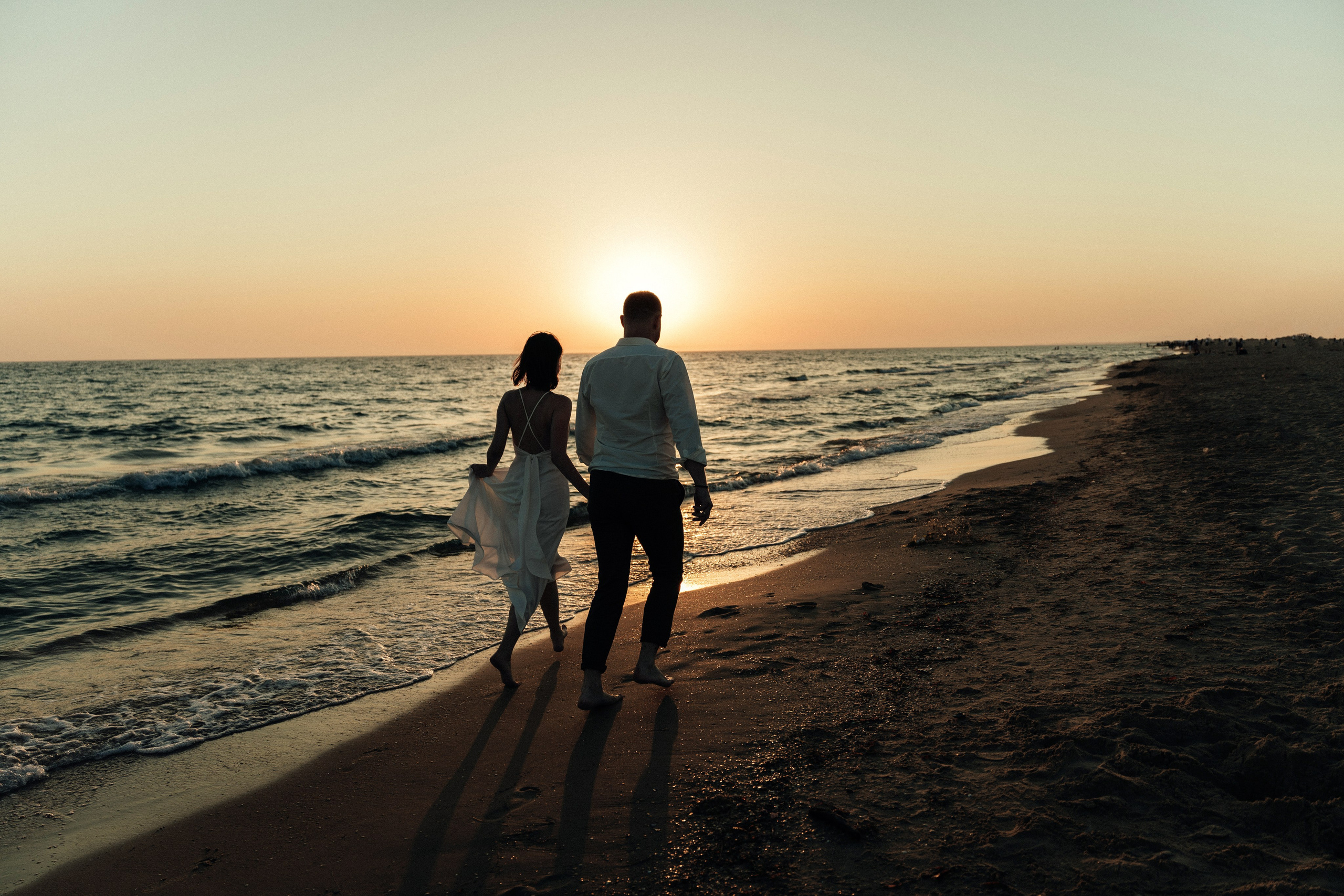 Пара гуляет вдоль моря на закате, песчаный пляж, романтика