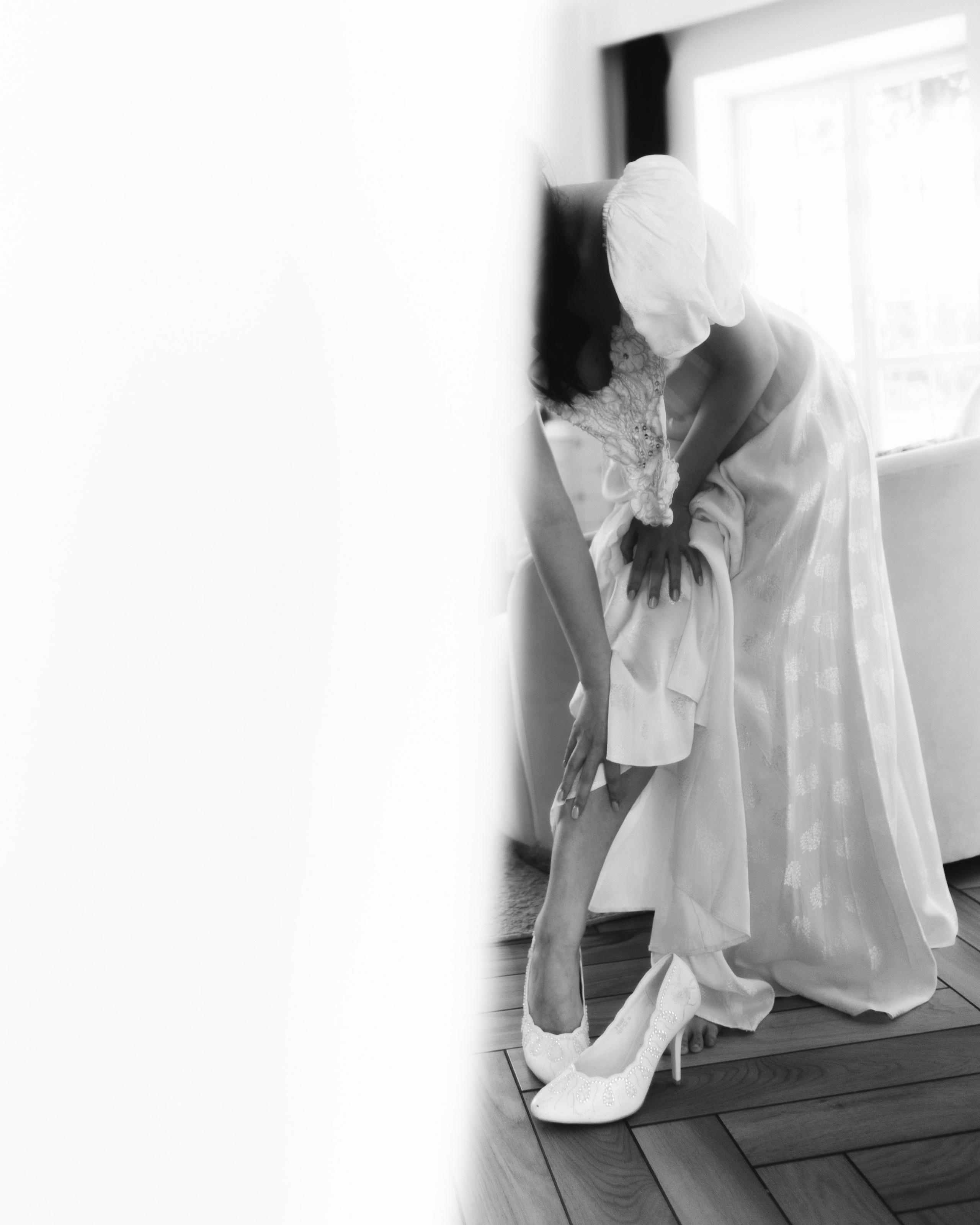 Черно-белая фотосессия утра невесты, невеста надевает туфли у окна, атмосферный свадебный кадр