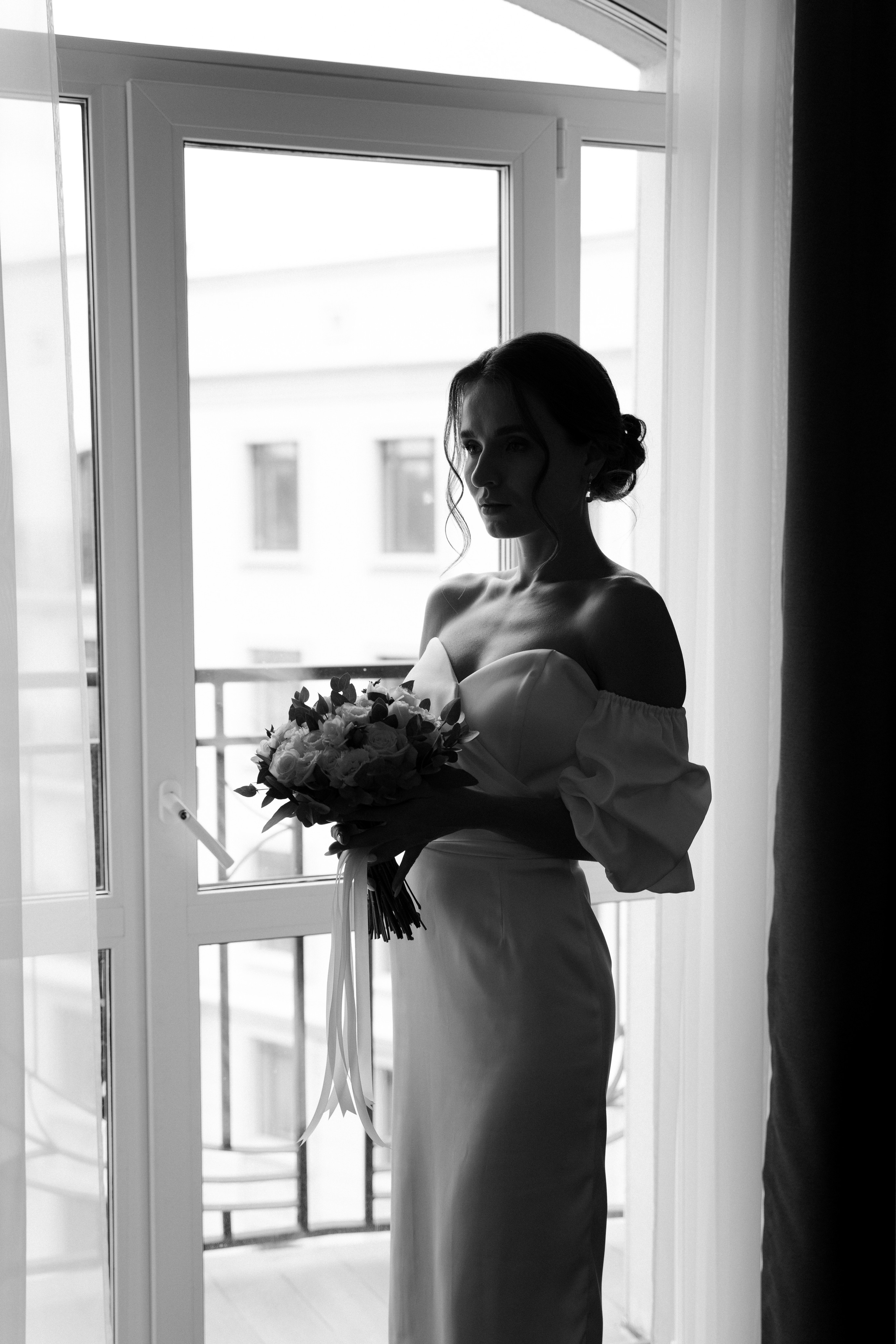 Невеста в белом платье с букетов цветов у окна.