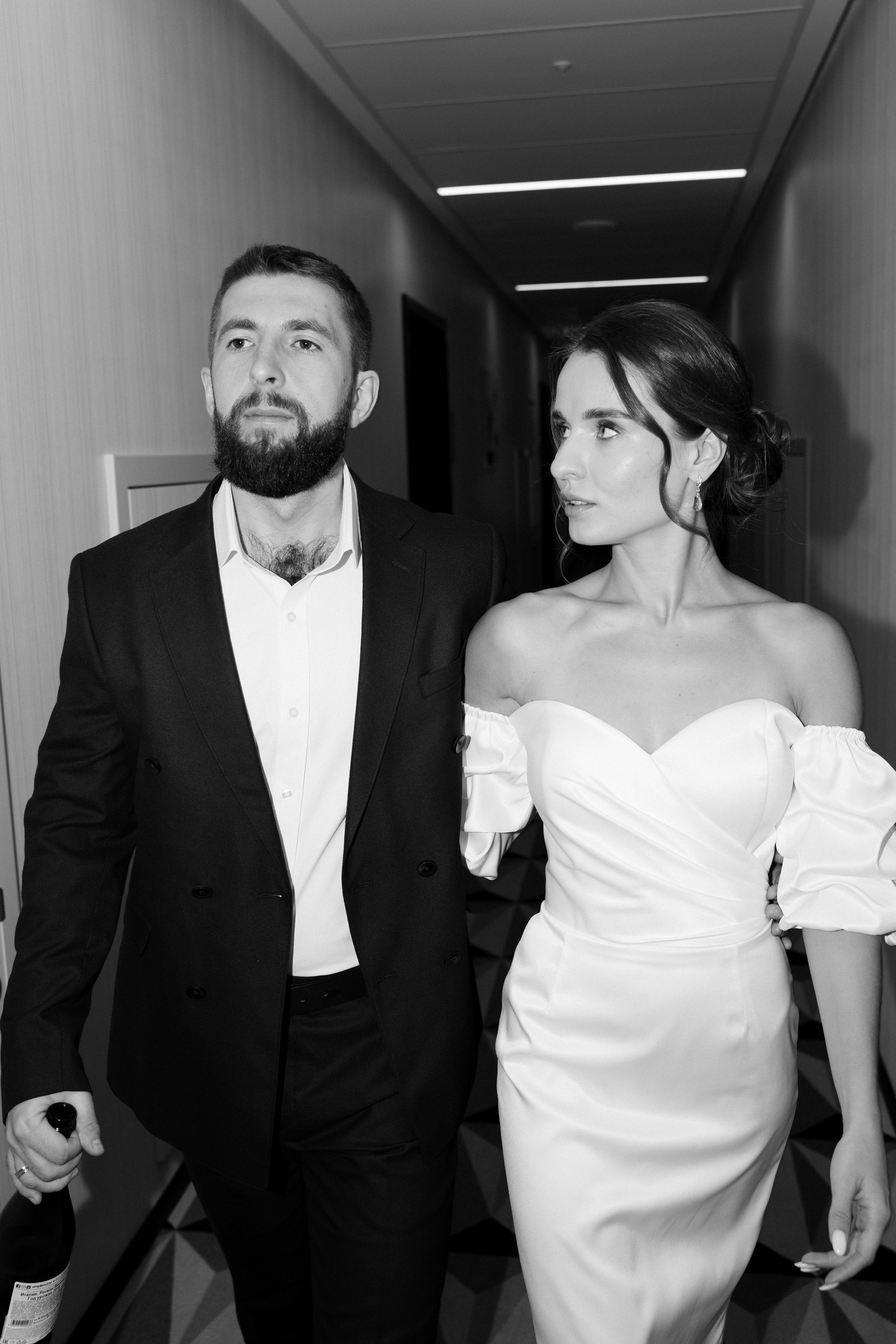 Жених и невеста в коридоре отеля идут с бутылкой и обнимаются