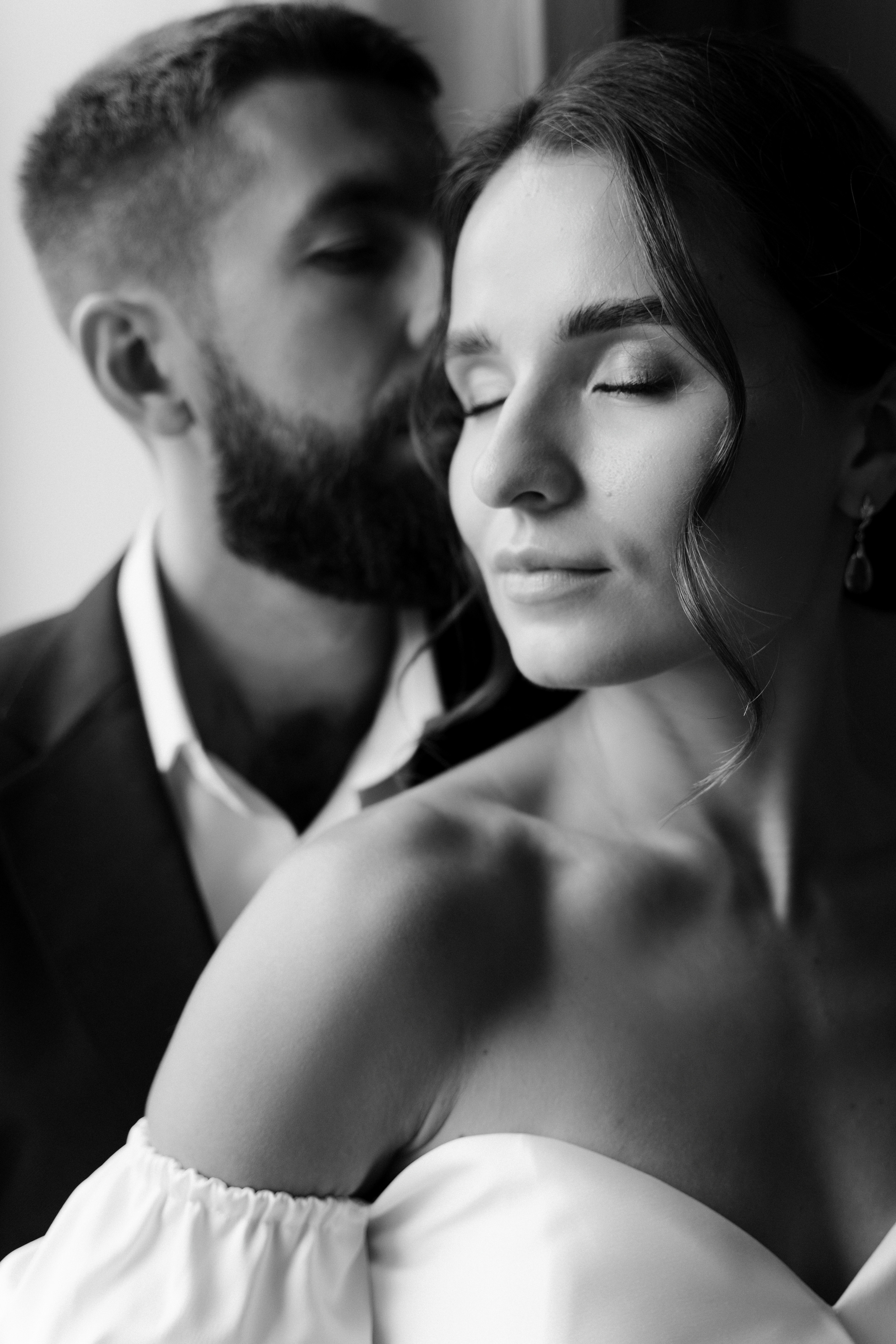 Портрет жениха и невесты в черно-белом цвете у окна. Жених целует невесту