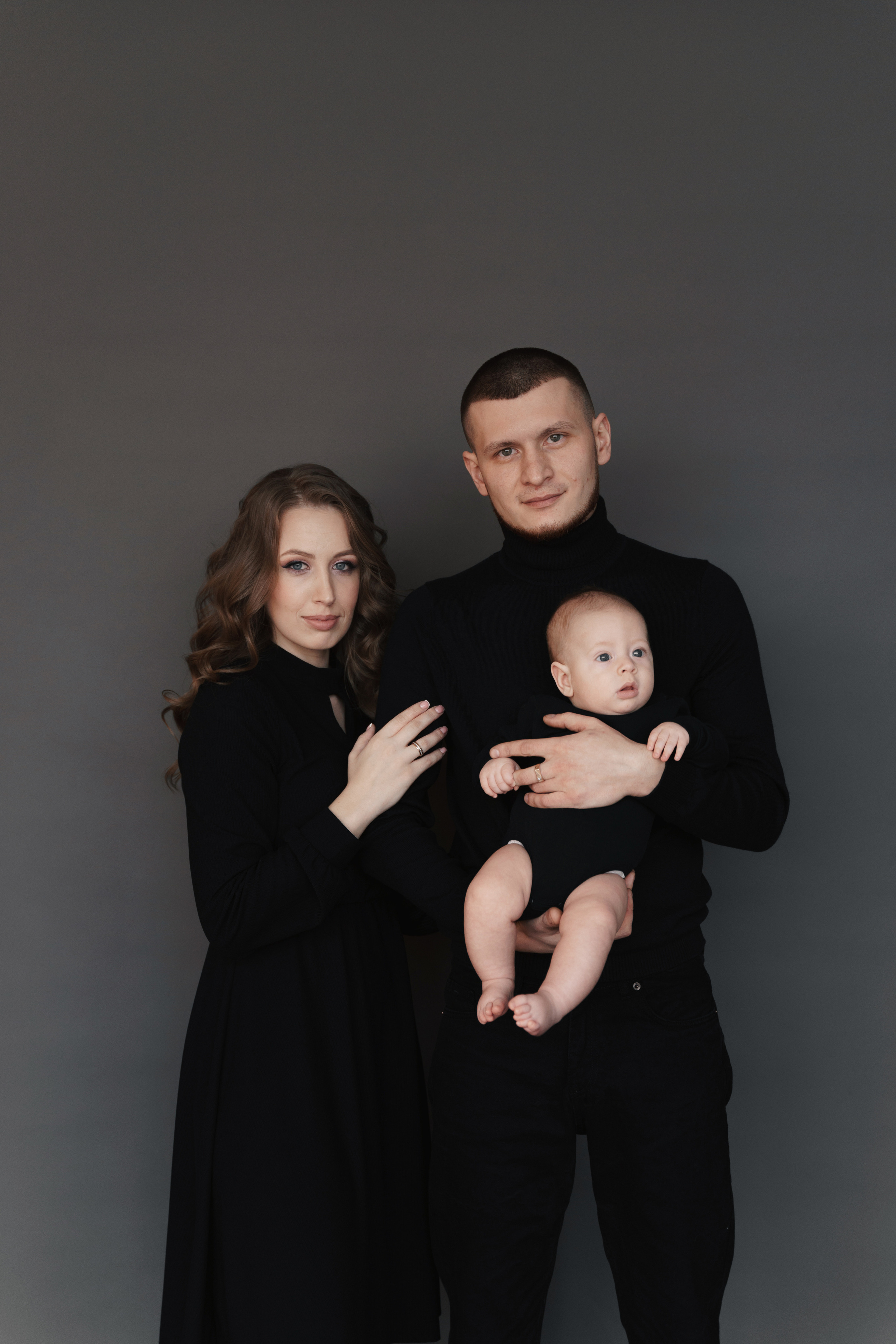 Семья из трех человек на сером фоне стоит с ребенком