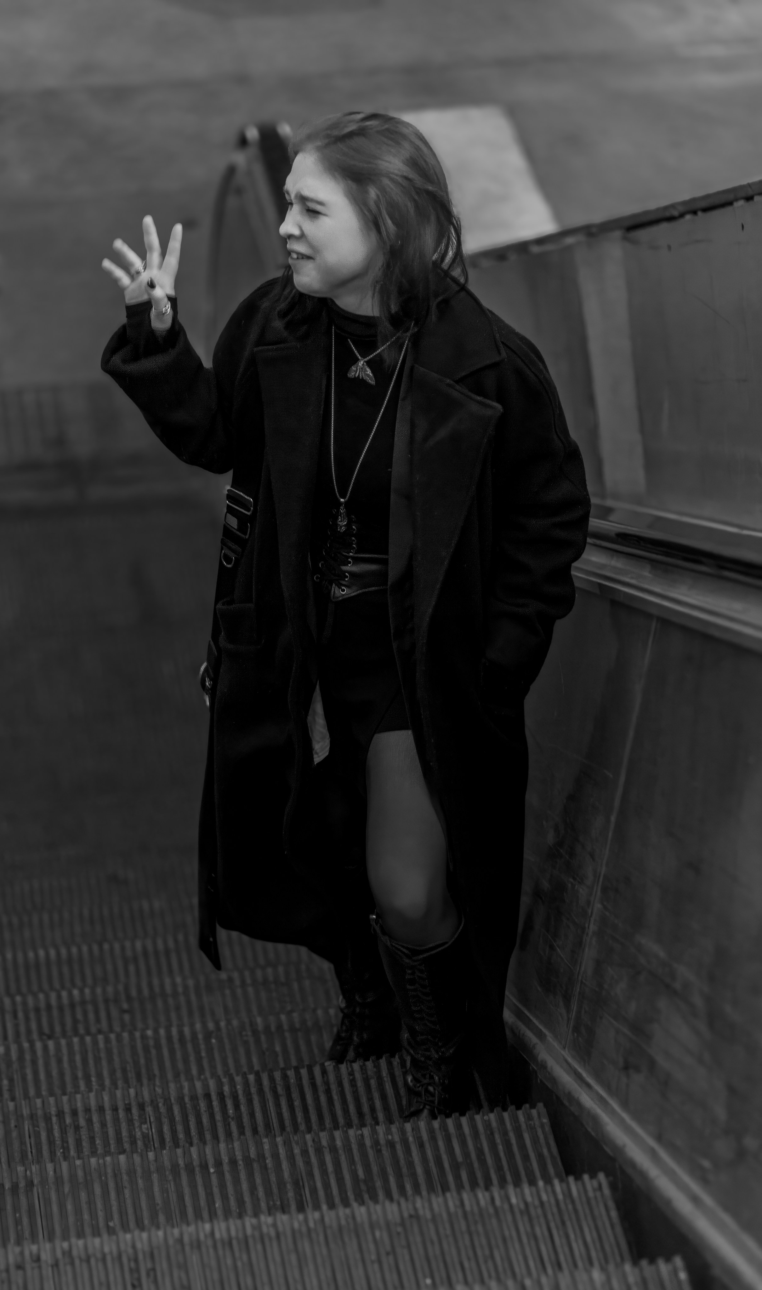 Черно-белый портрет девушки,  стоящей на ступеньках эскалатора и машушей кому-то рукой