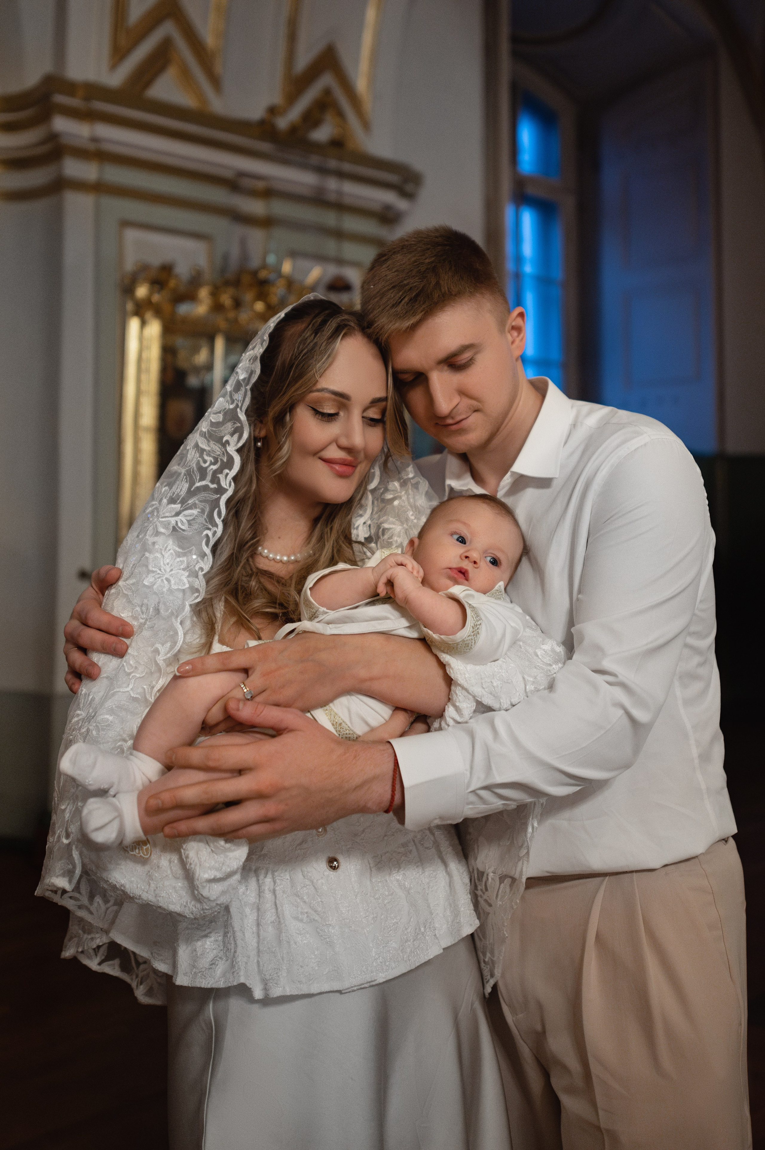 папа обнимает маму с малышом после крещения в Николо-Богоявленском соборе Санкт-Петербурга