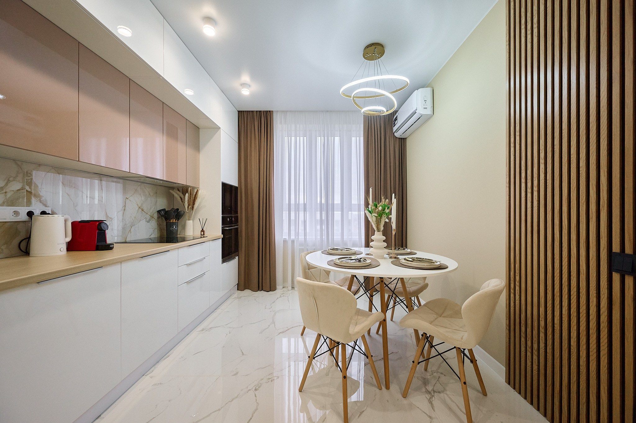 кухня в современном стиле белые шкафы коричневые оттенки  белый кухонный стол и светлые стулья 