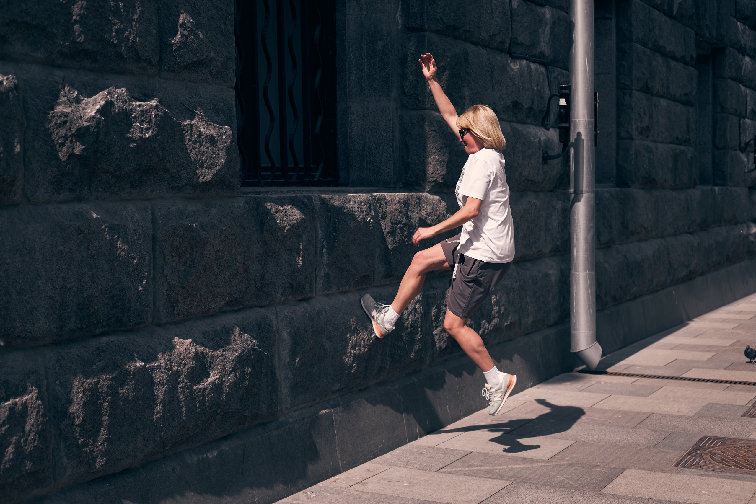 Девушка в шортах и белой футболке отталкиваясь от стены прыгает