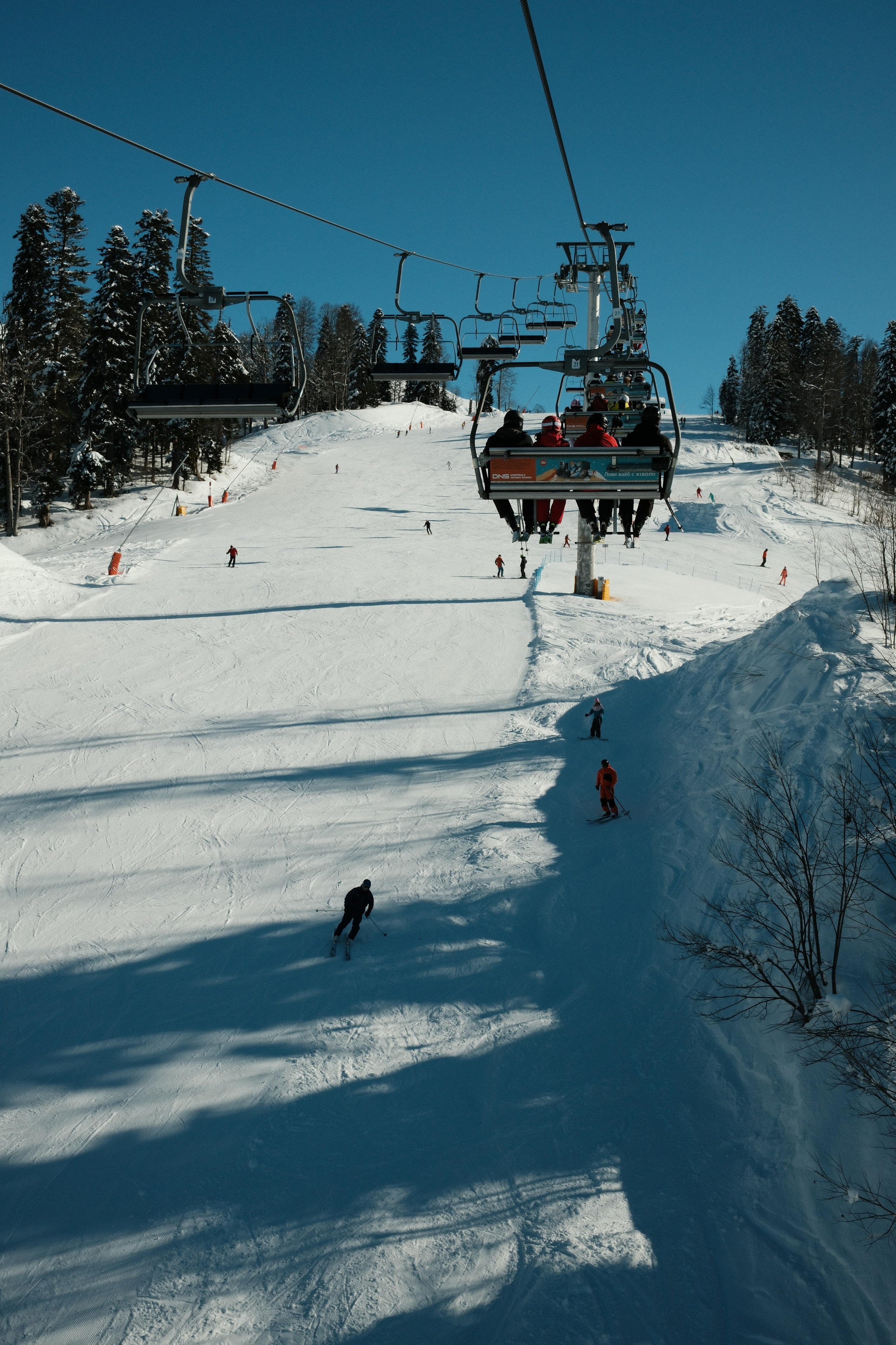 На переднем плане кресельный подъемник с горнолыжниками, по склону едут горнолыжники