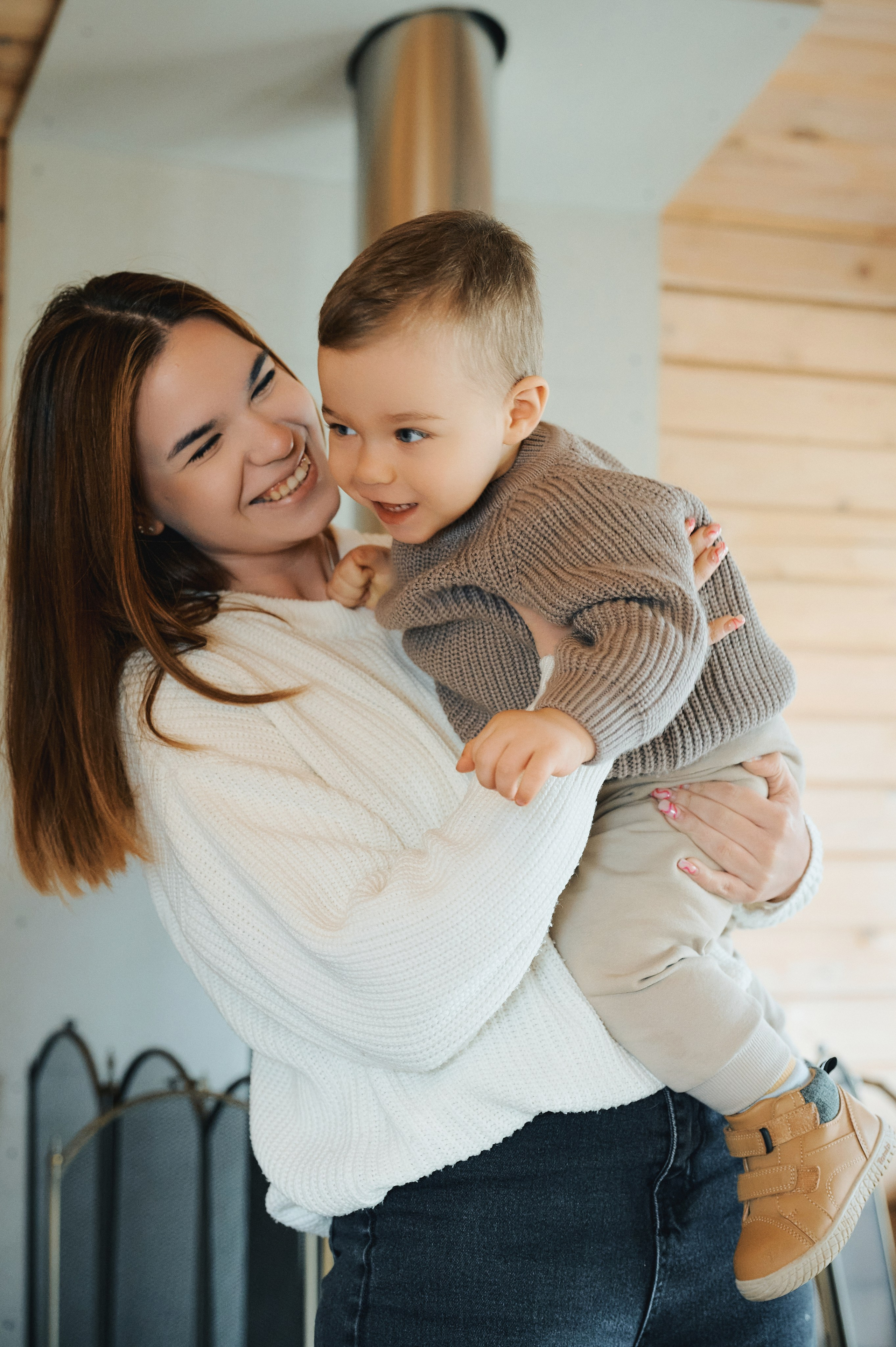 мама держит сына на руках, оба улыбаются, светлый интерьер деревянного дома