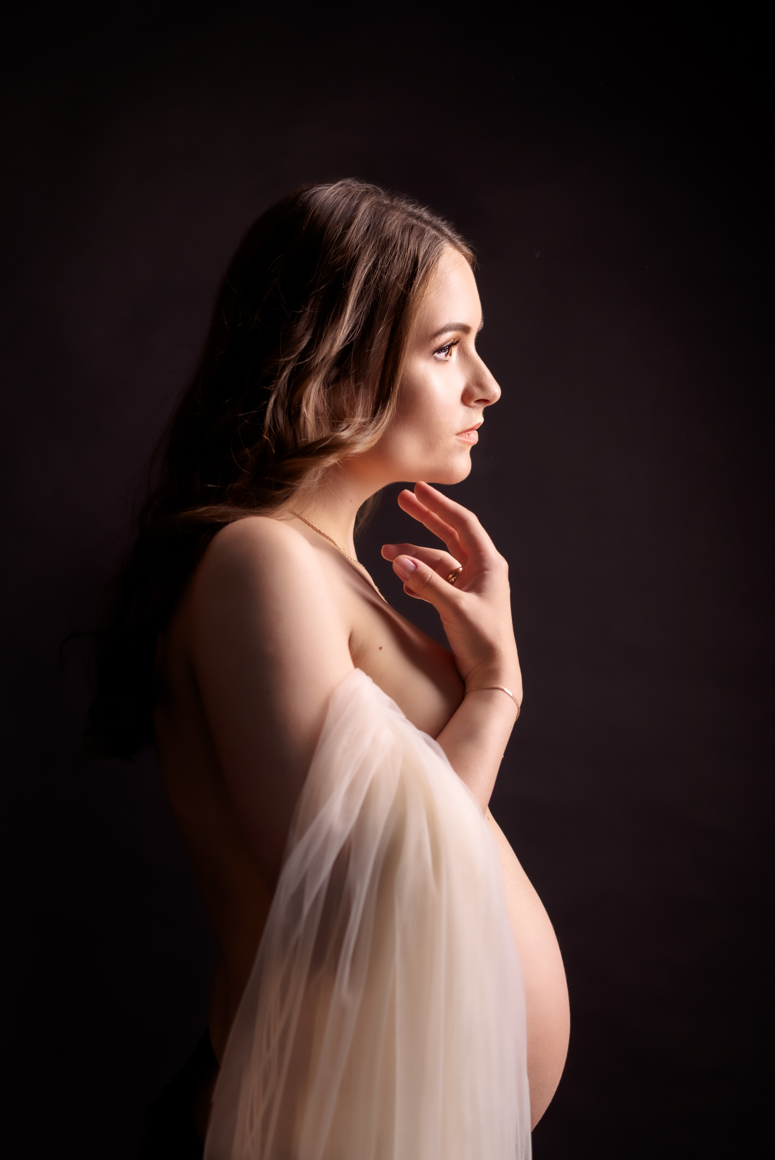 обнаженная беременная женщина с прозрачной легкой тканью на черном фоне