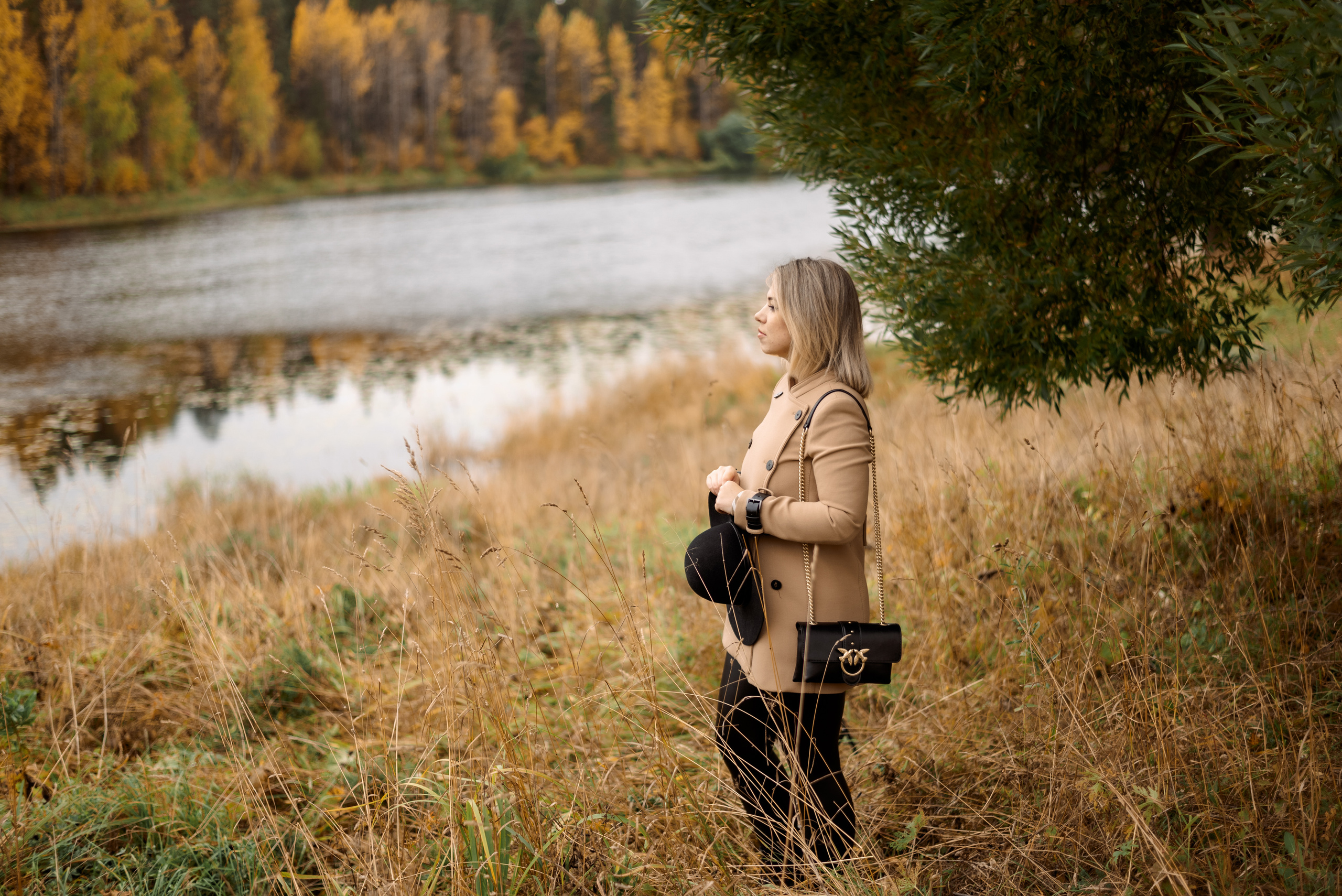 девушка стоит на берегу озера в сухой траве на фоне осеннего леса