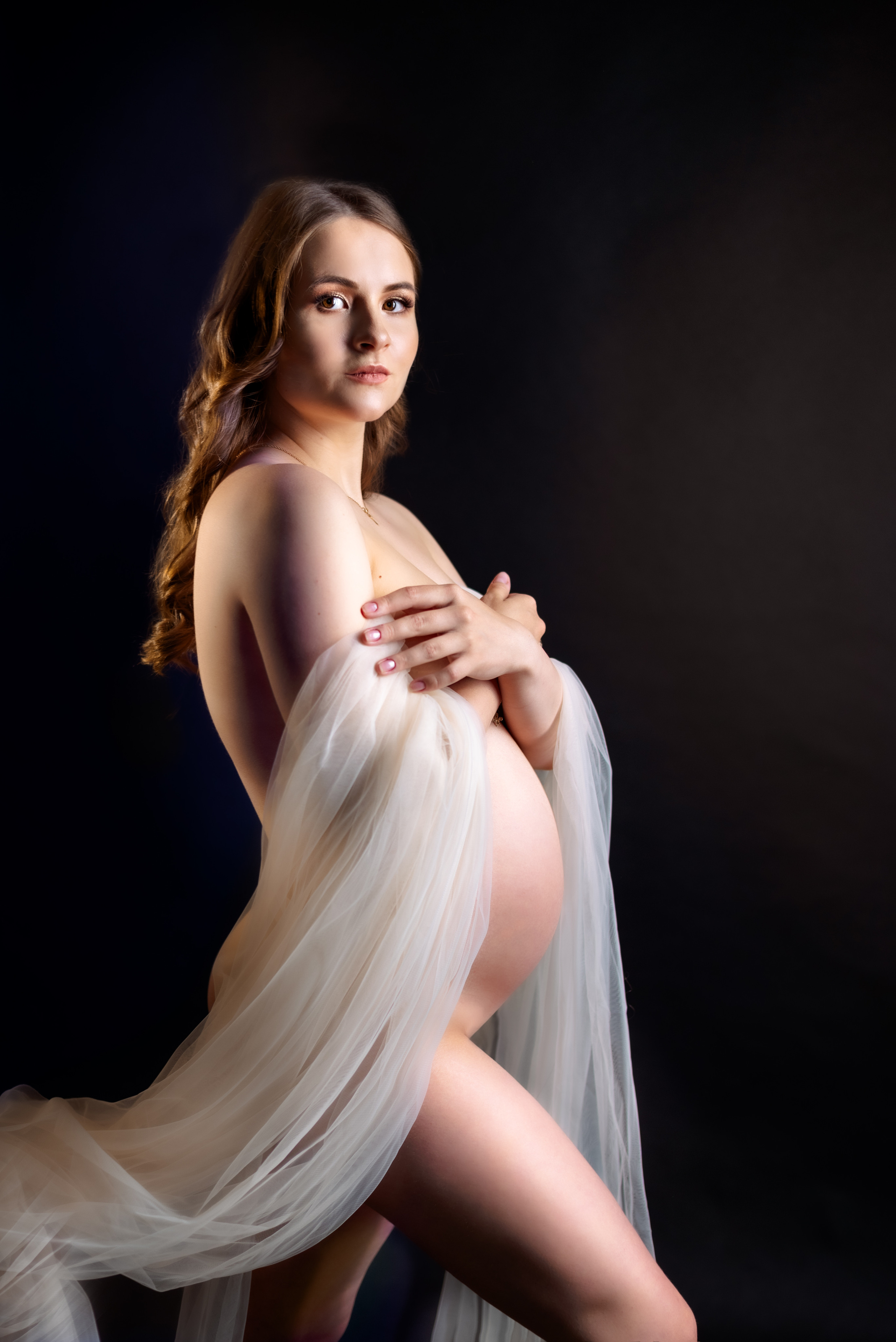 обнаженная беременная женщина с прозрачной легкой тканью на черном фоне