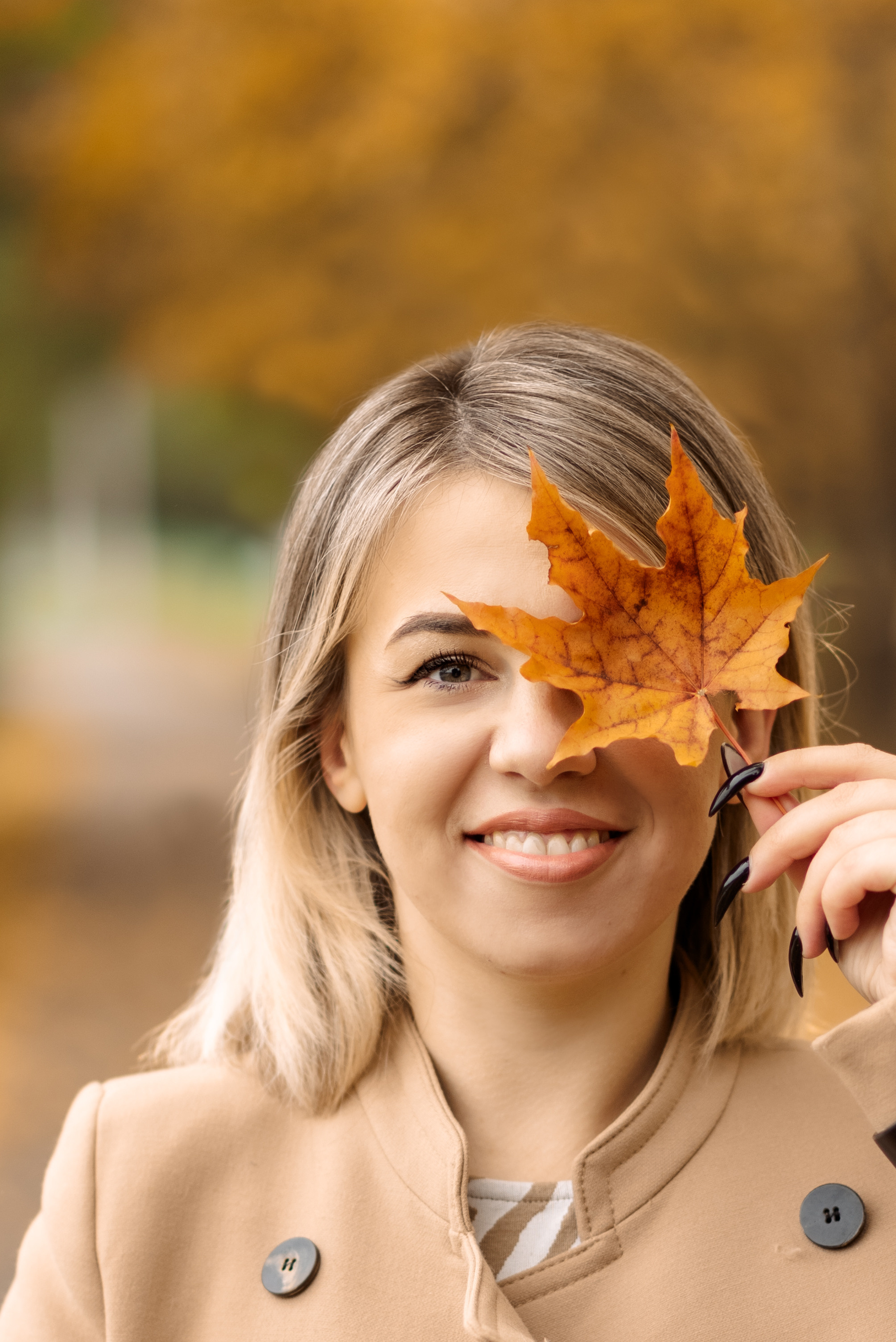 девушка в осеннем парке часть лица закрывает кленовым листом 