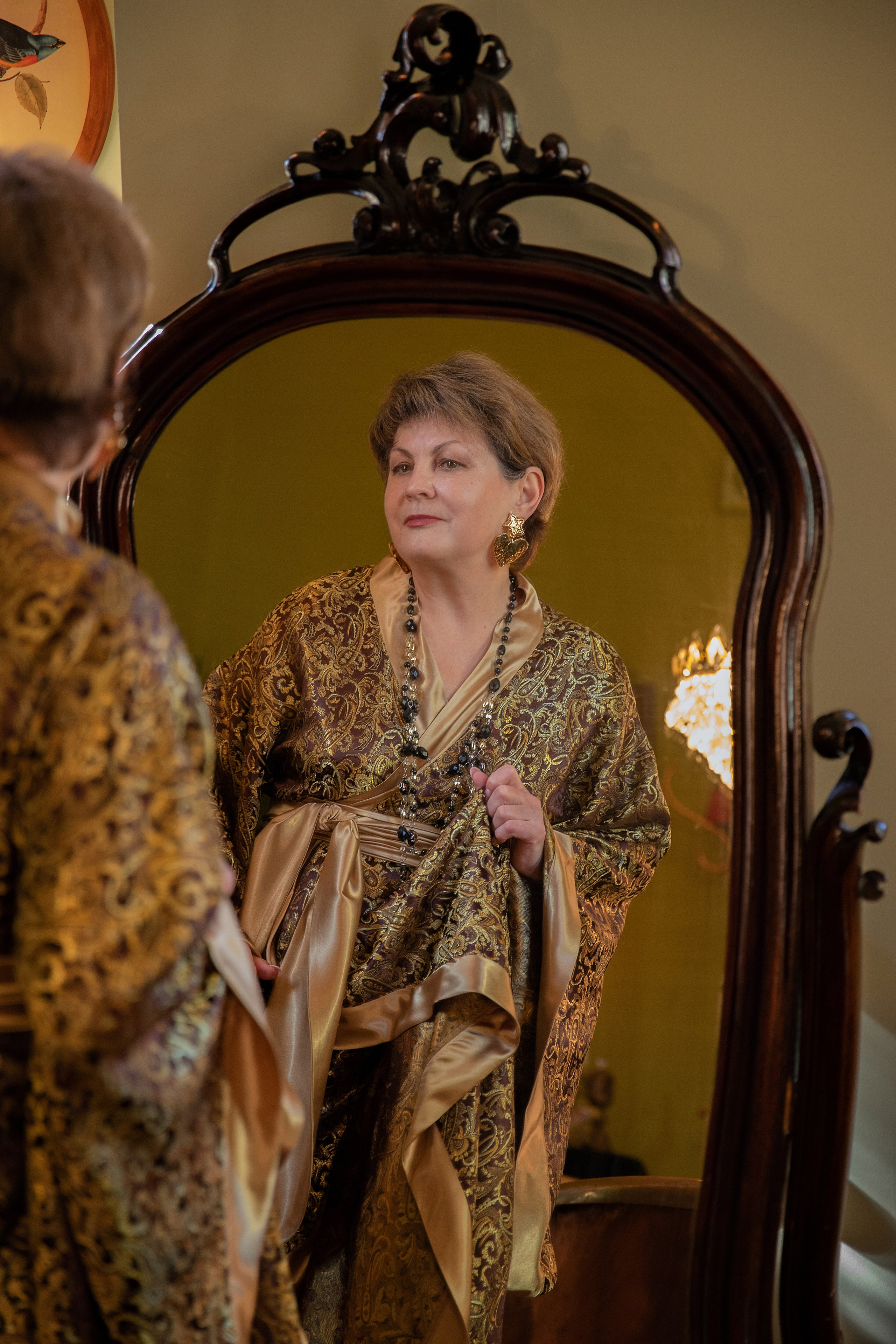 Словно символ вечной красоты, женщина в удивительном пеньюаре тихо наслаждается моментом в уюте традиционного будуара, подчеркивая свою грацию и стиль.