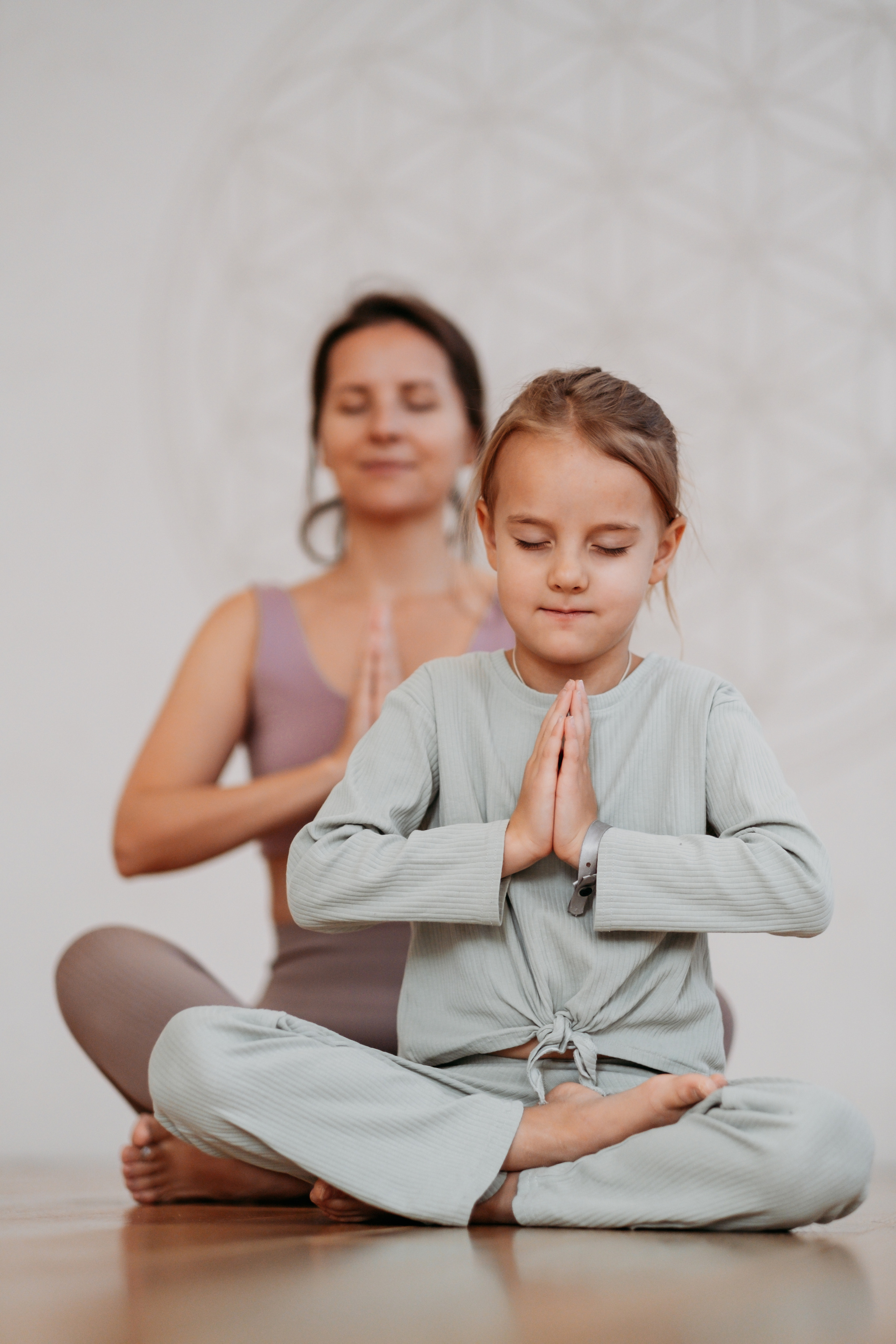 Мама и дочь сидят в позе йога и делают намасте