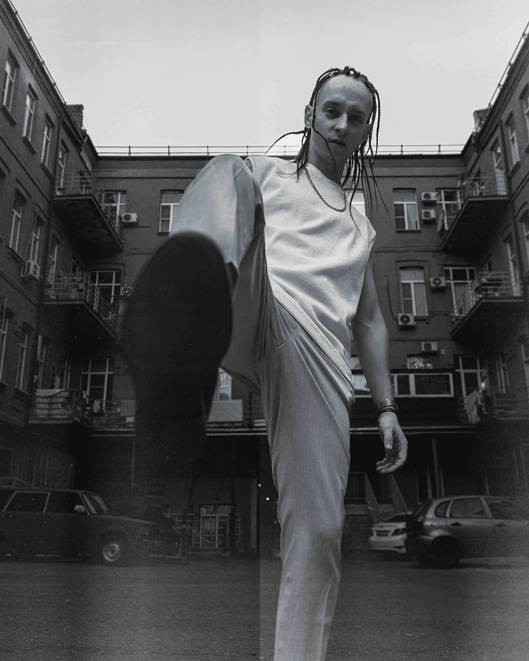 Чёрно белый мужской портрет, в котором мужчина замахивается ногой в камеру 