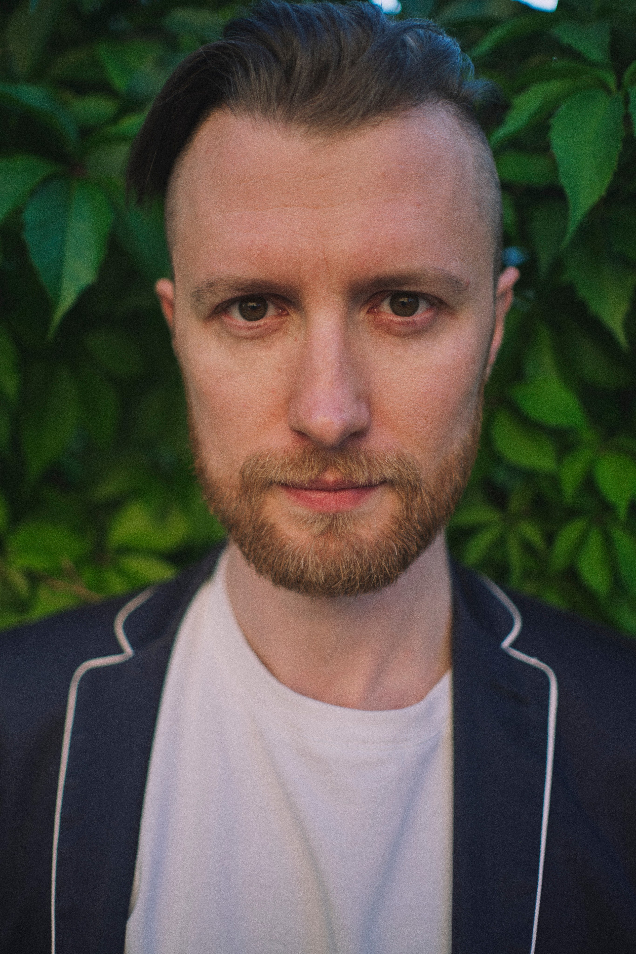 Очень близкий портрет мужчины в пиджаке на фоне дикого винограда