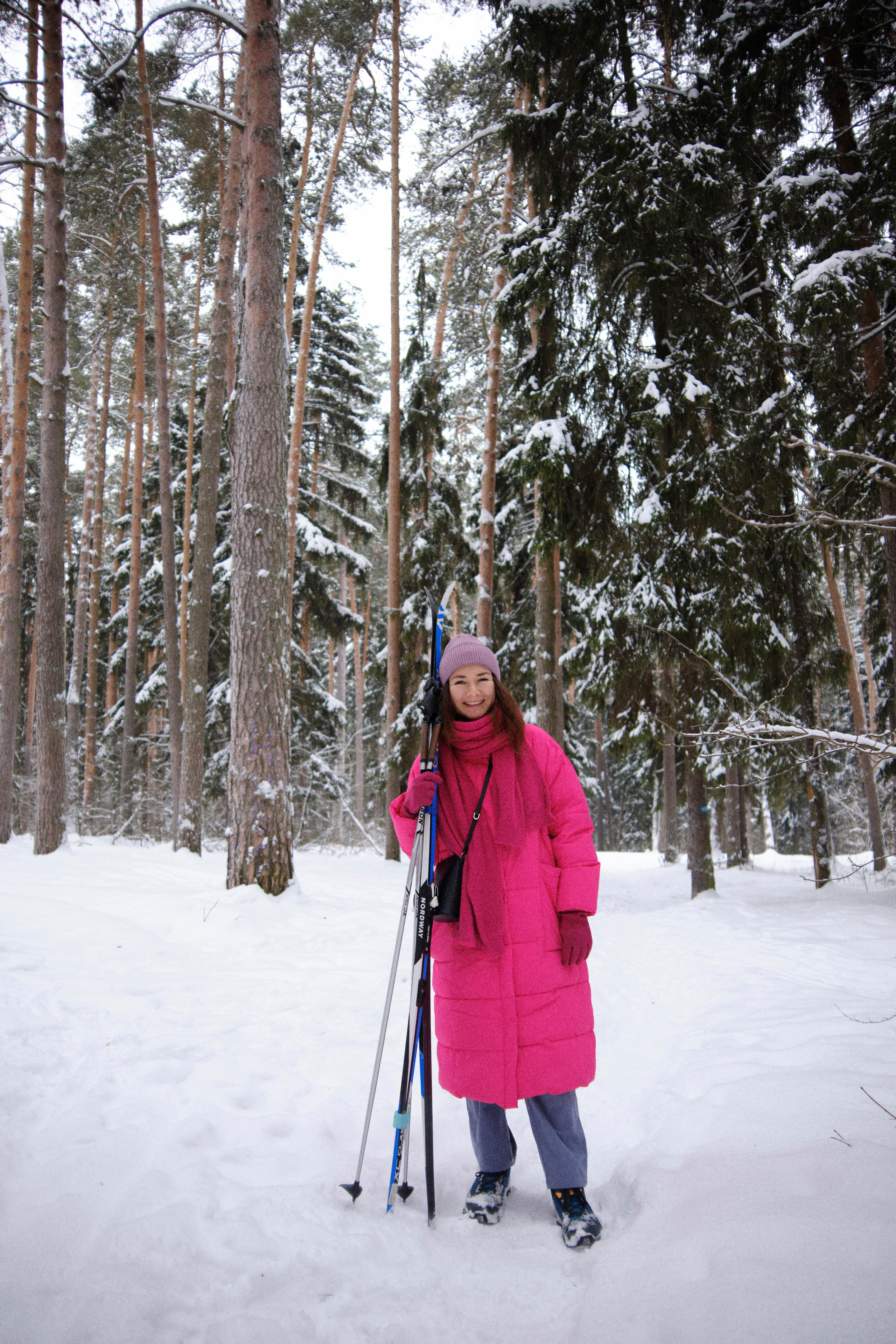 Девушка в яркой одежде стоит с лыжами в заснеженном лесу