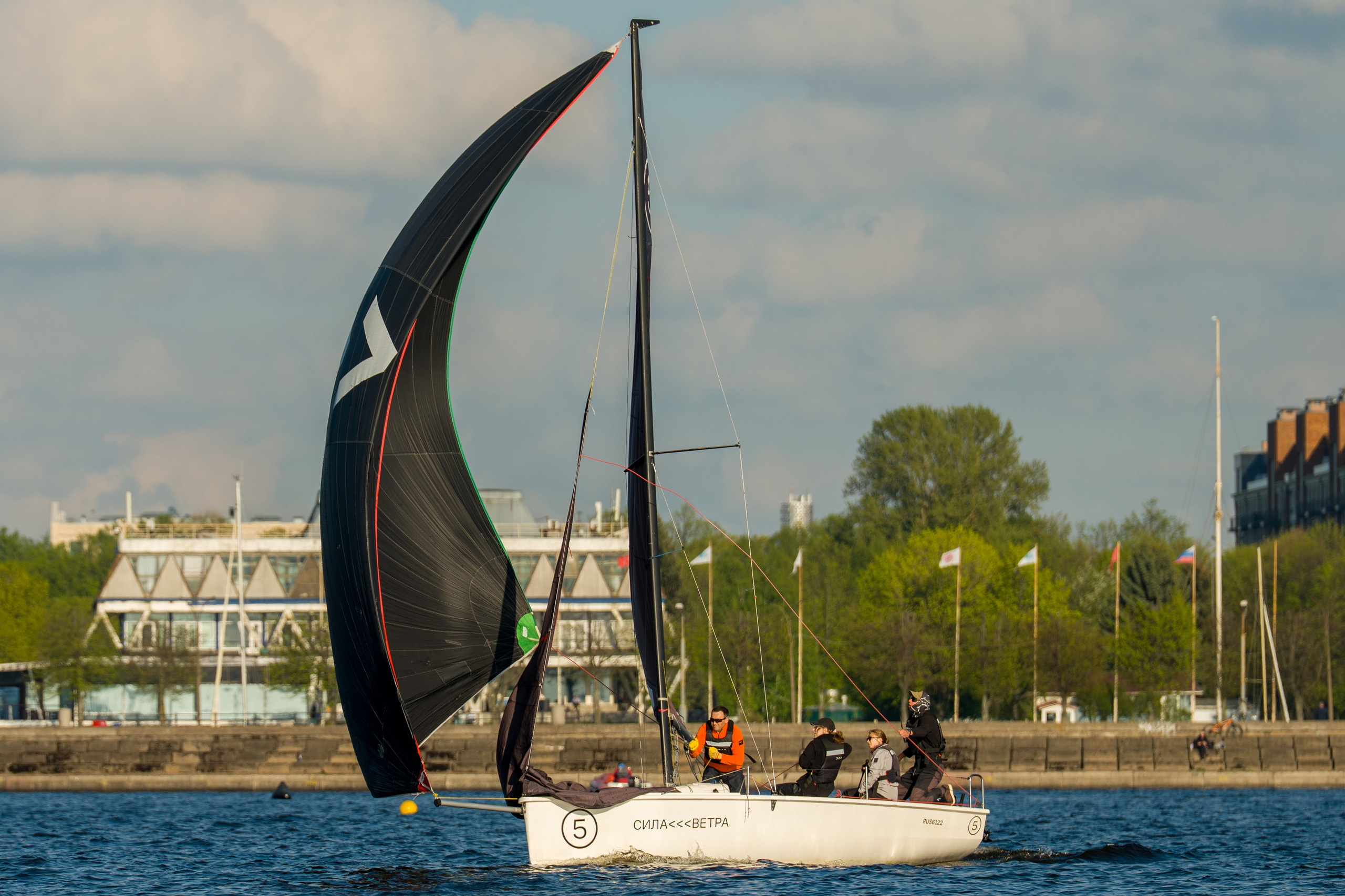 SV20 crew hoists a black spinnaker, trimming hard off St Petersburg quay