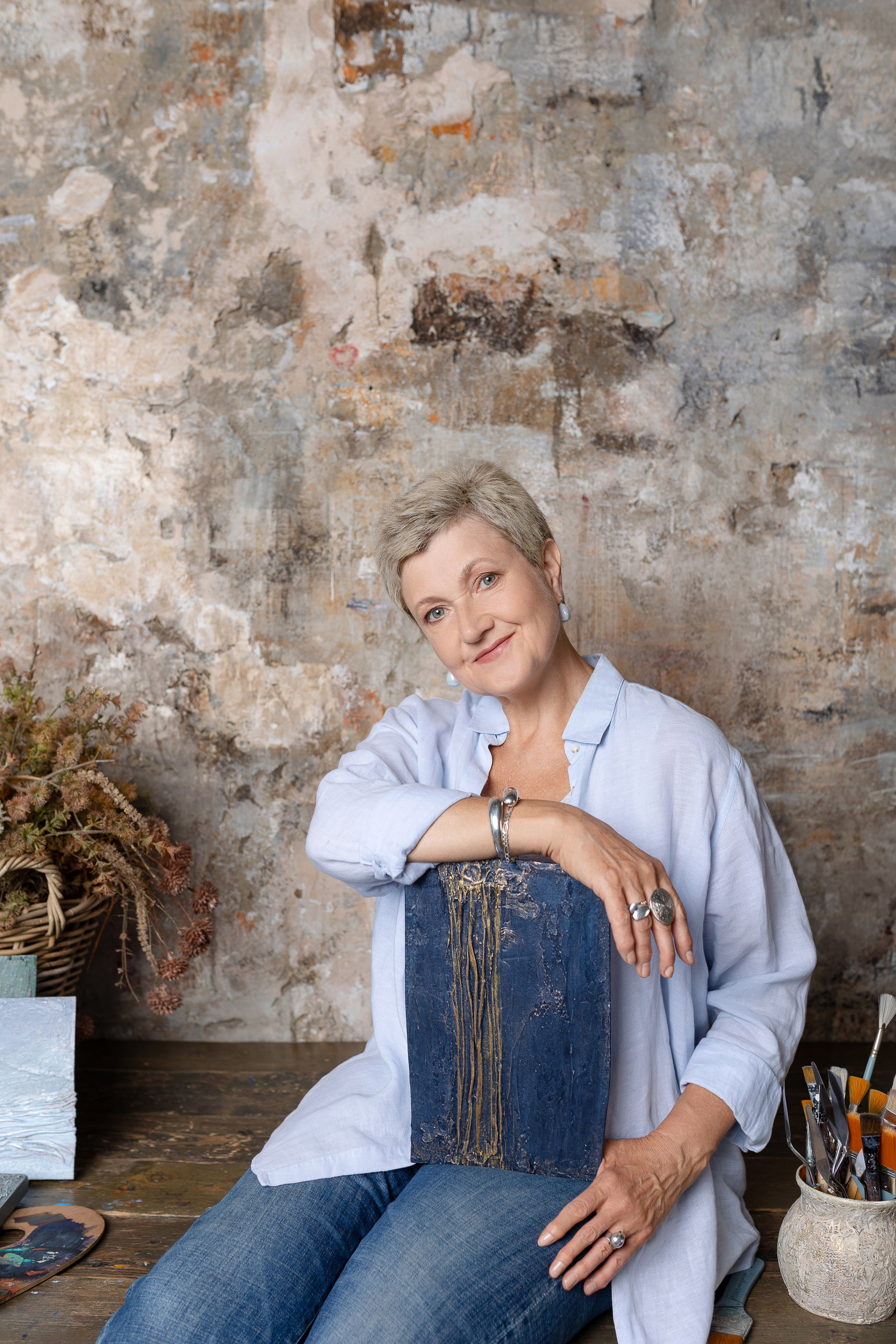 На фоне стены сидит художница, правой рукой облокотившись на картину.