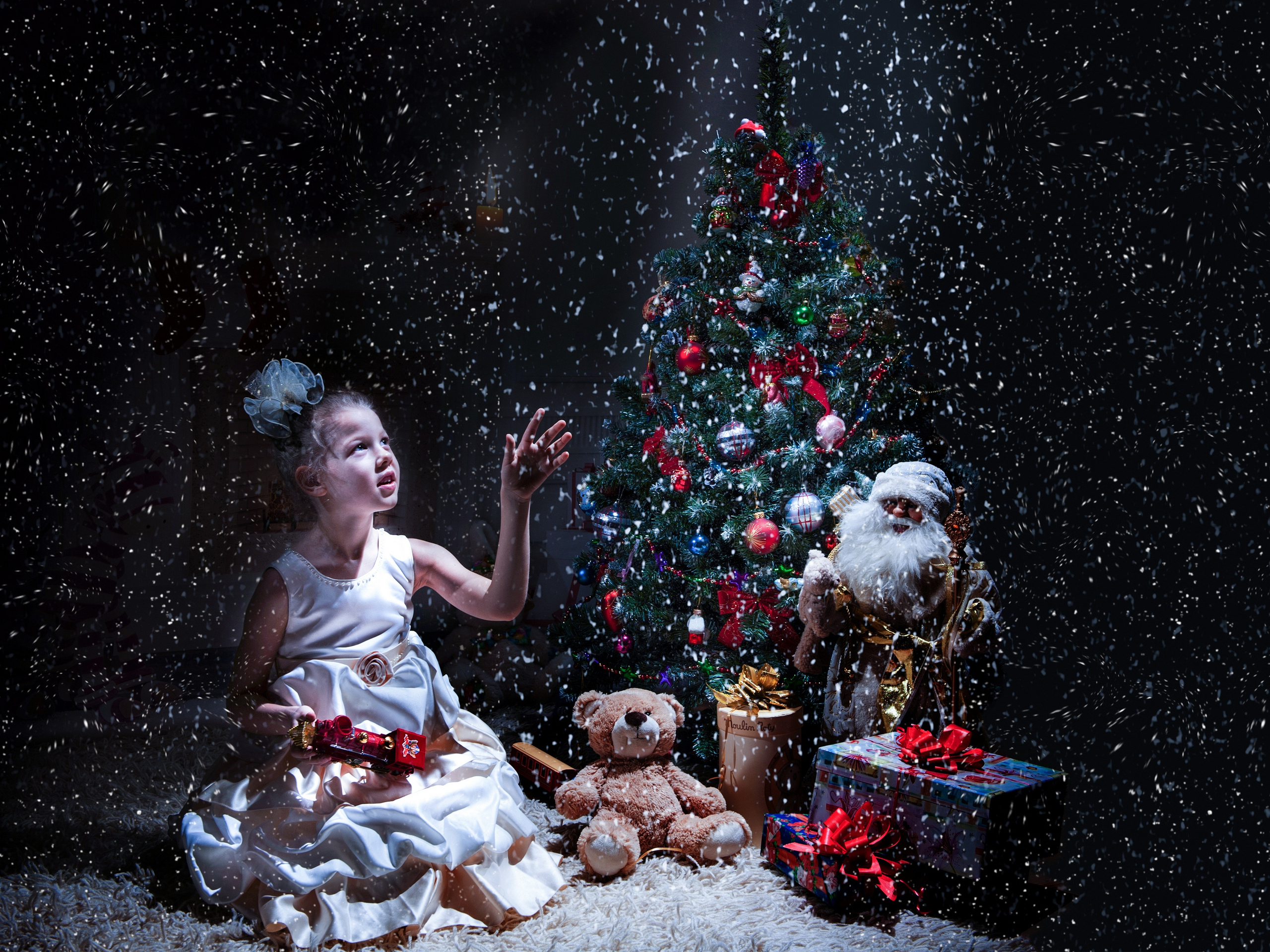 девочка сидит на полу на фоне новогодней елки и ловит рукой снежинки