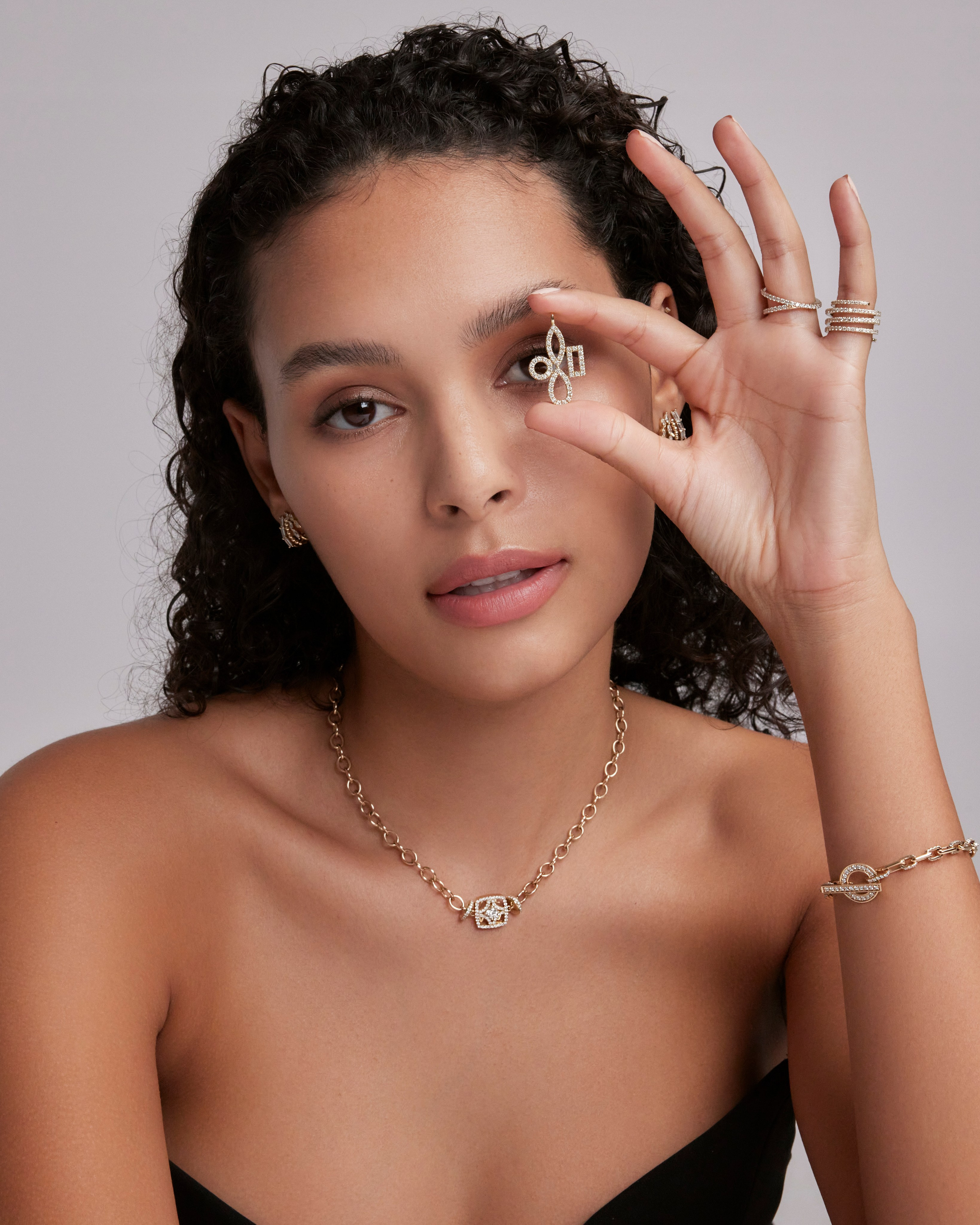 Curly-haired model showcasing a gold ring and delicate necklace, emphasizing modern elegance in jewelry.