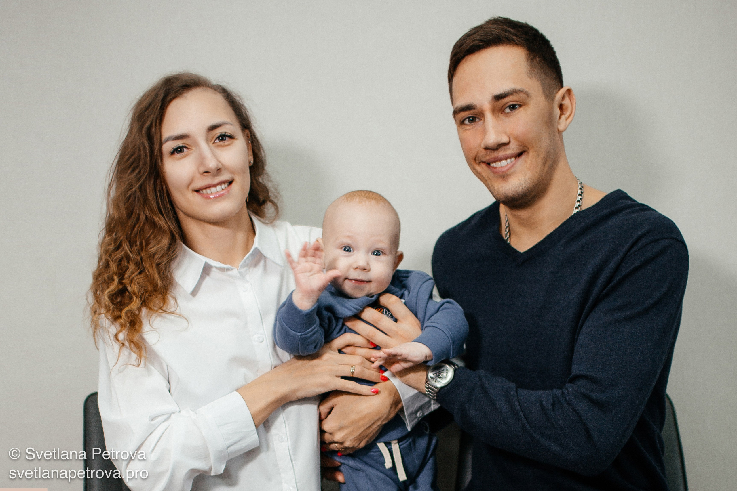 Семейная фотосессия — родители и малыш. Счастливая семья в студии, улыбка ребёнка. Родители держат малыша, тёплый кадр. Семья из трёх человек, радость. Малыш между мамой и папой, весёлый взгляд. Семейная гармония — родители с ребёнком. Улыбки родителей, любопытный малыш в центре.