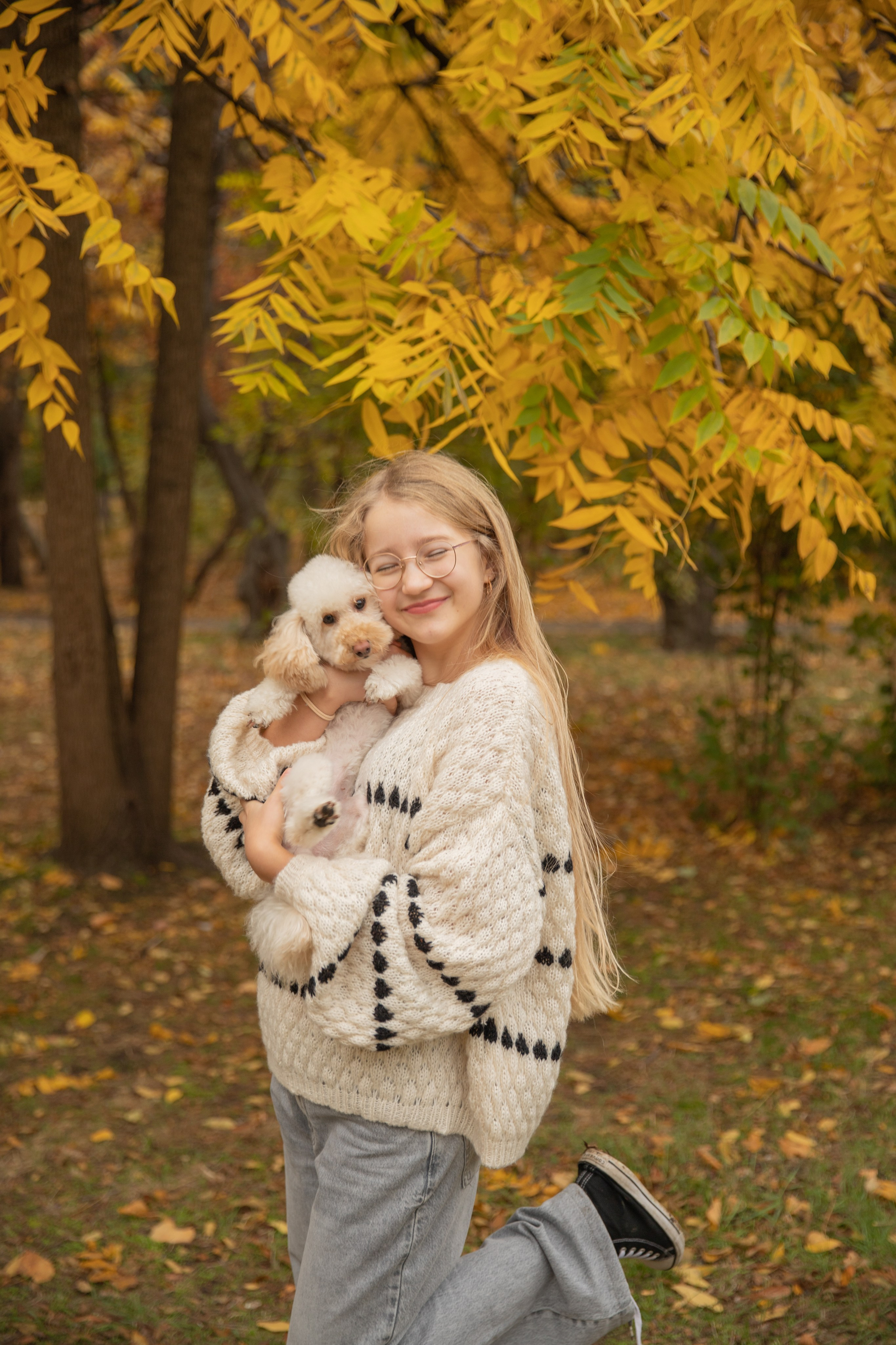 Улыбающиеся девочка  держат в руках любимую собачку гна фоне  красочной осенней природы парка Чистяковская роща.