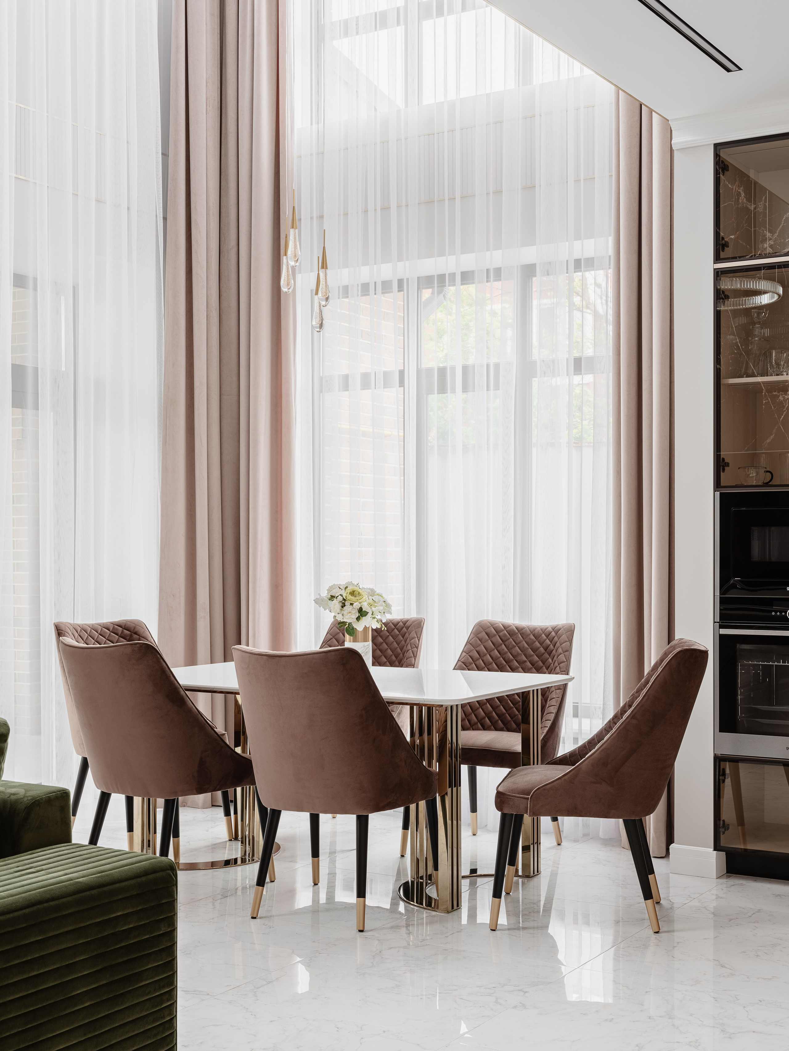 Элегантный ракурс столовой с высоким остеклением, мягкими бежево-розовыми шторами и бархатными креслами, белый глянцевый стол и золотые акценты, дизайнер Евгения Ермошина, фотограф Сергей Денисенко.