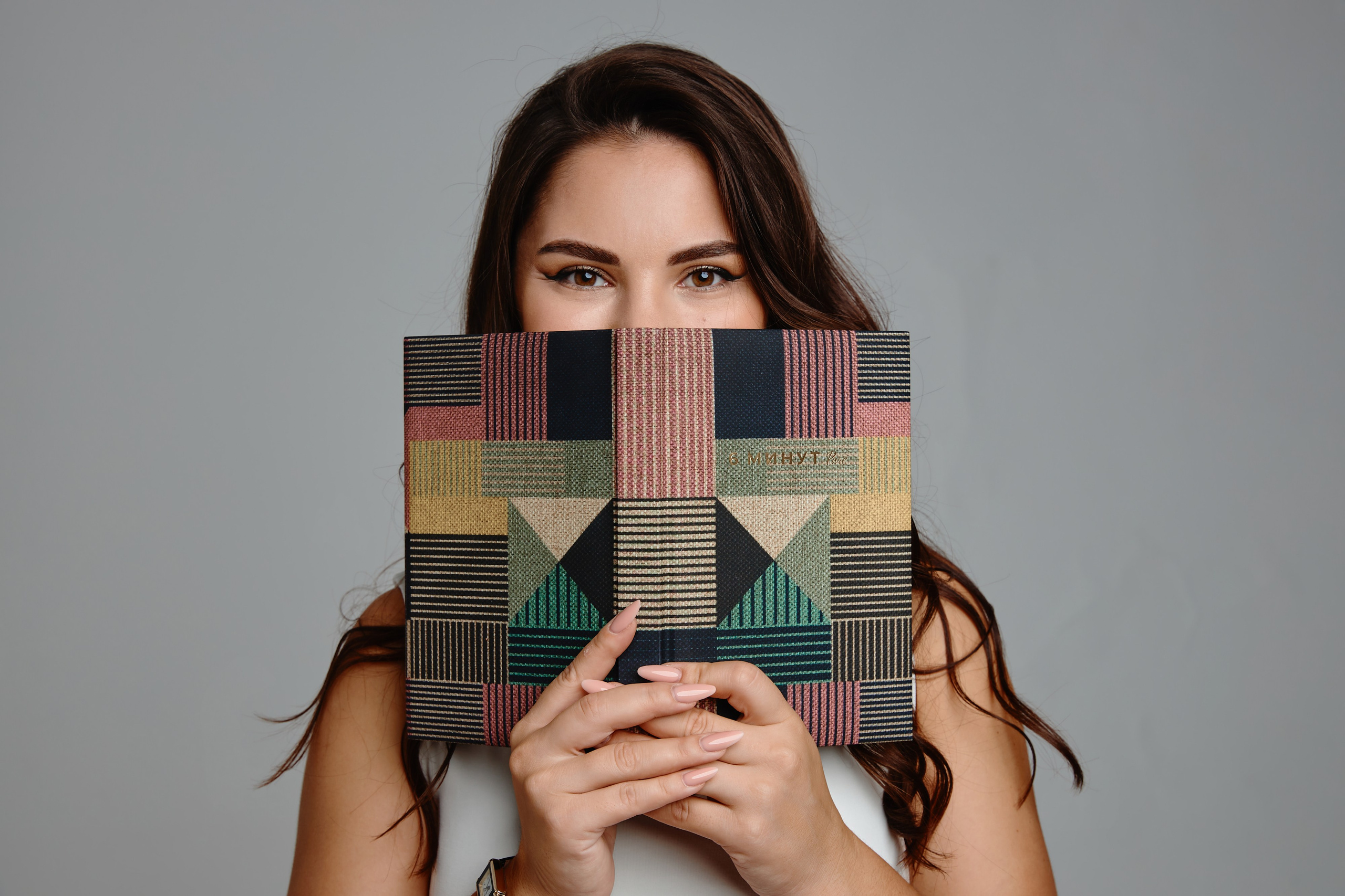 Девушка улыбается прячет лицо за книгу