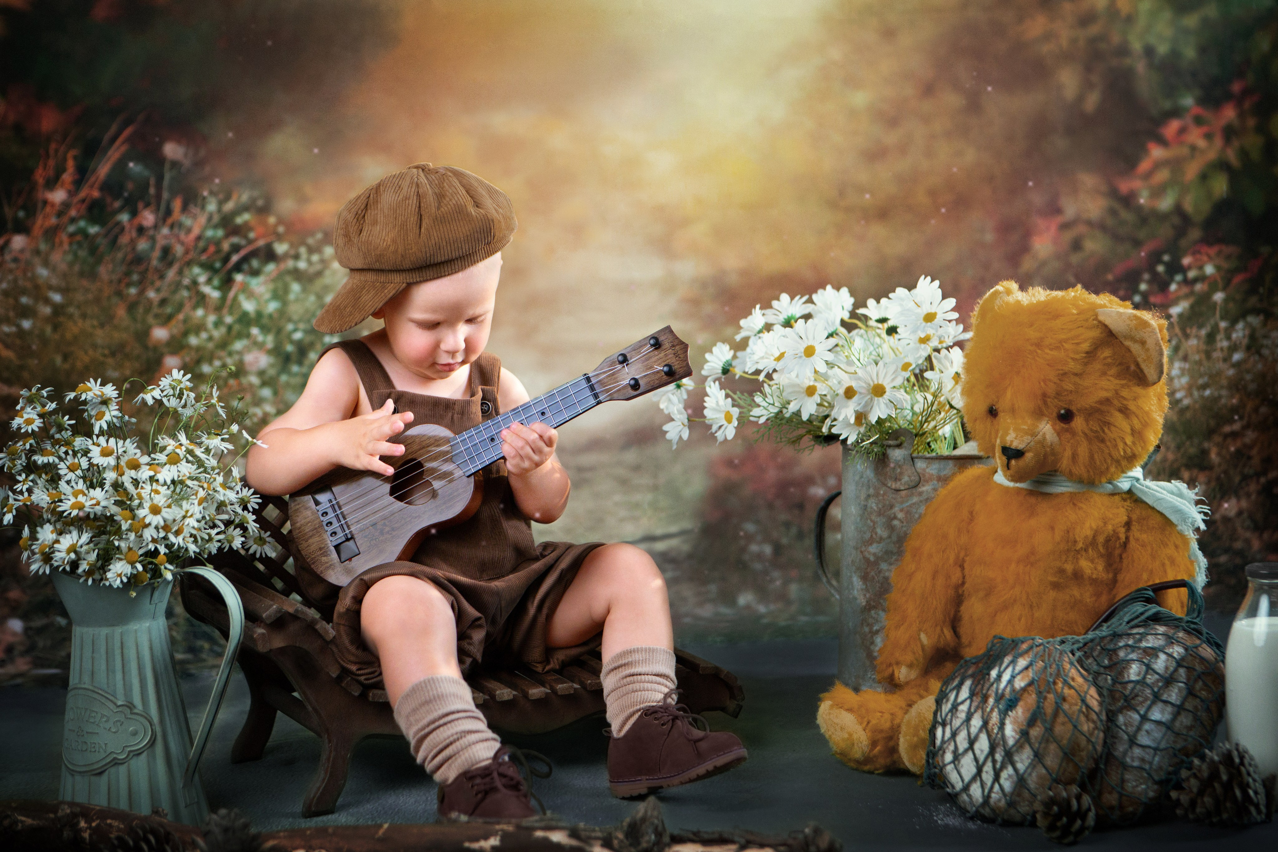 Малыш играет на гитарке, вокруг него много ромашек и старинный медведь.