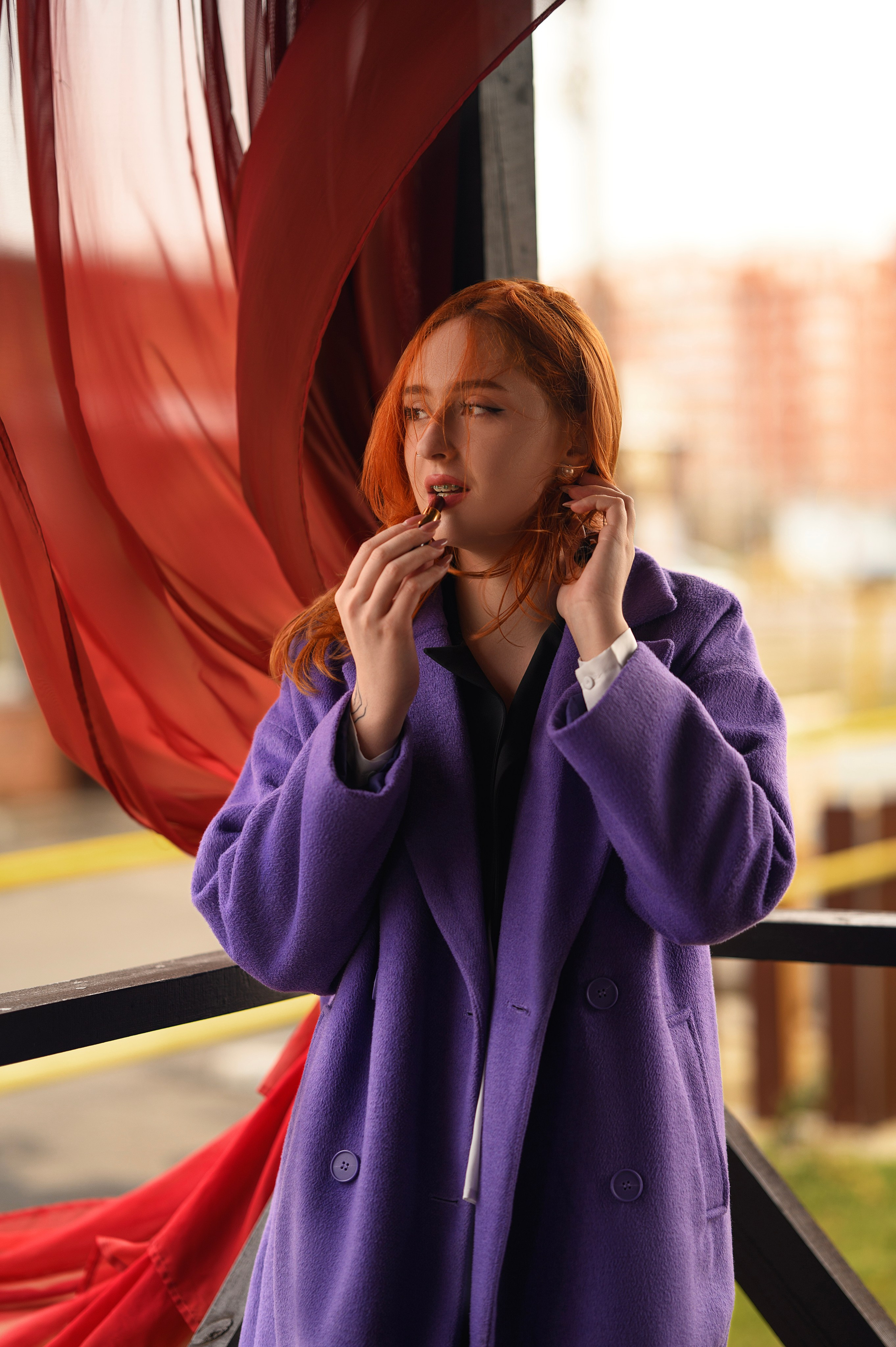 Фотосессия в Волгодонске от Елизаветы Жуйковой. Девушка в фиолетовом пальто, рыжие волосы, фон — здание с красными шторами.