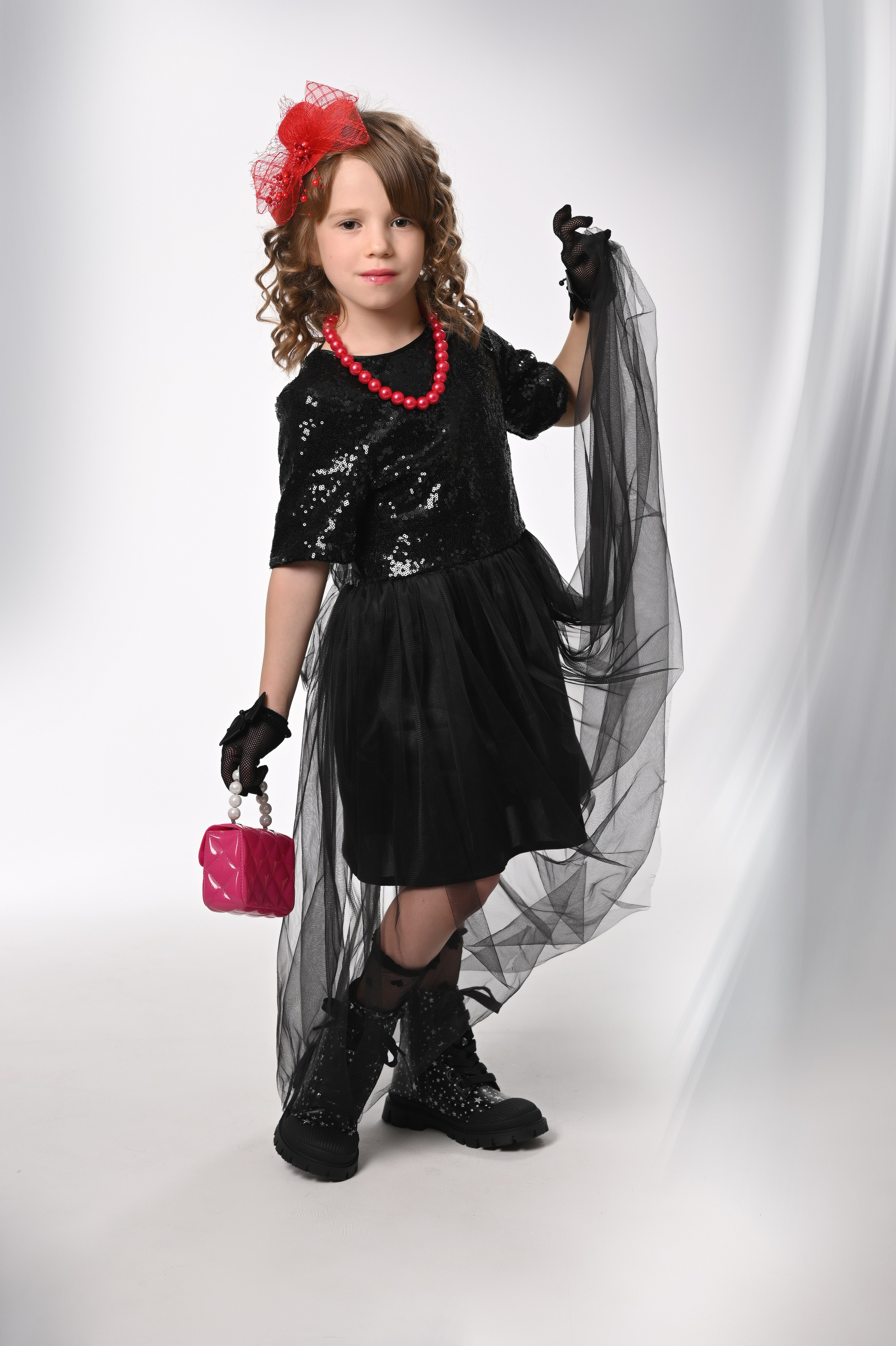 Девочка в выпускном платье и шапочке держит красную сумочку в фотостудии