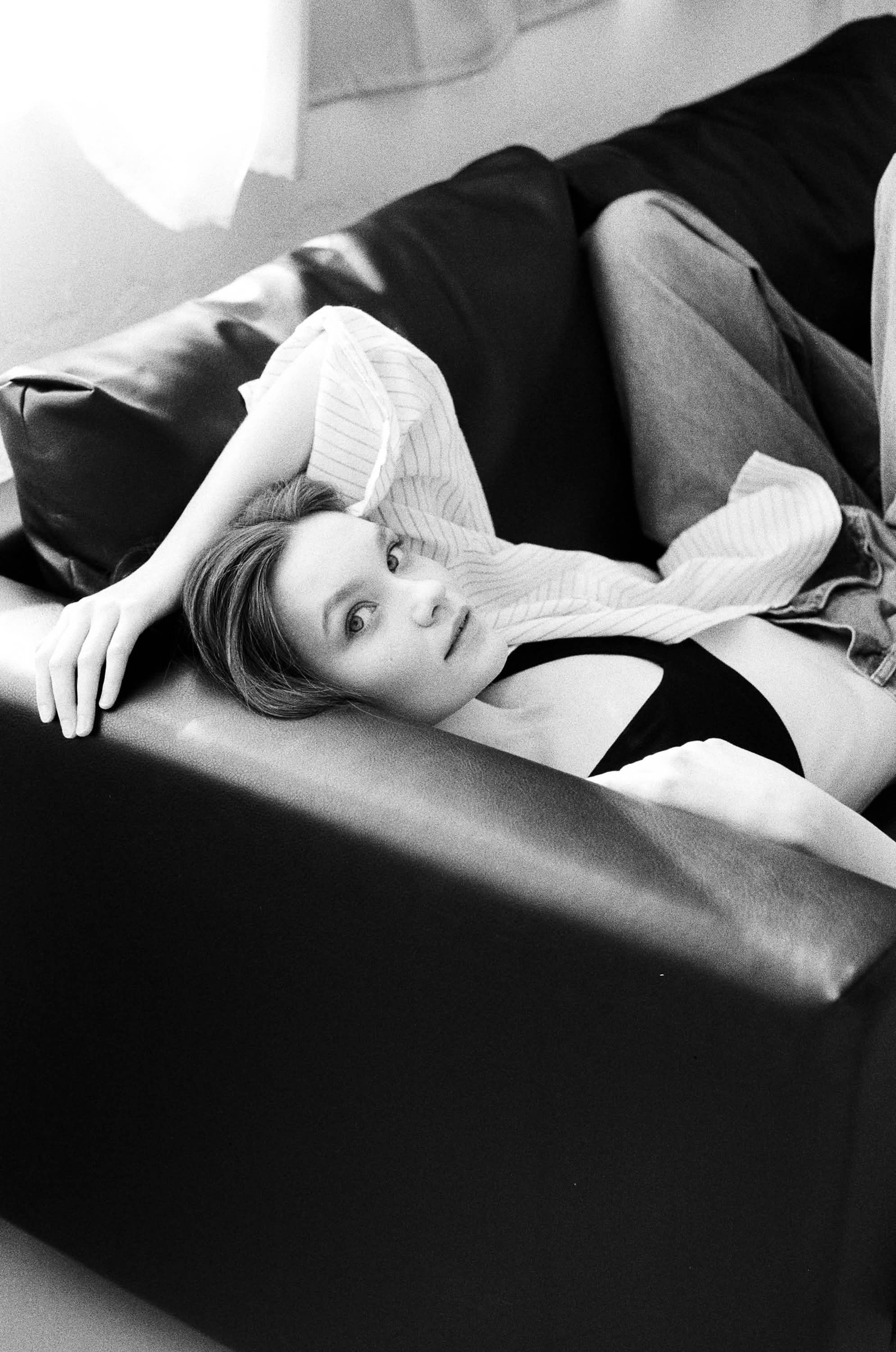 Фотосессия на плёнку СПб — чёрно-белый кадр девушки, расслабленно лежит на кожаном диване, мягкий контраст