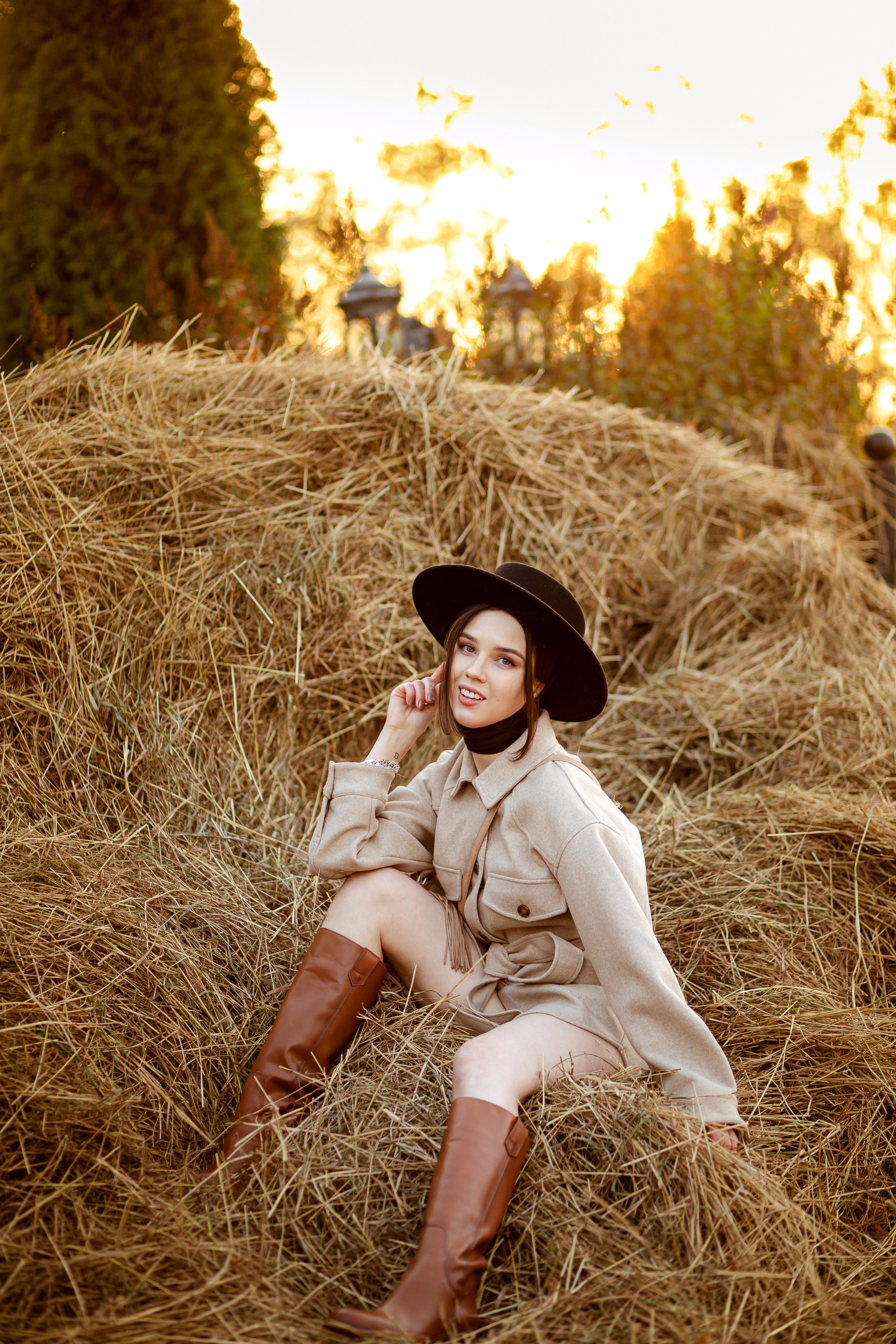 Девушка сидит на стоге сена на фоне заката.