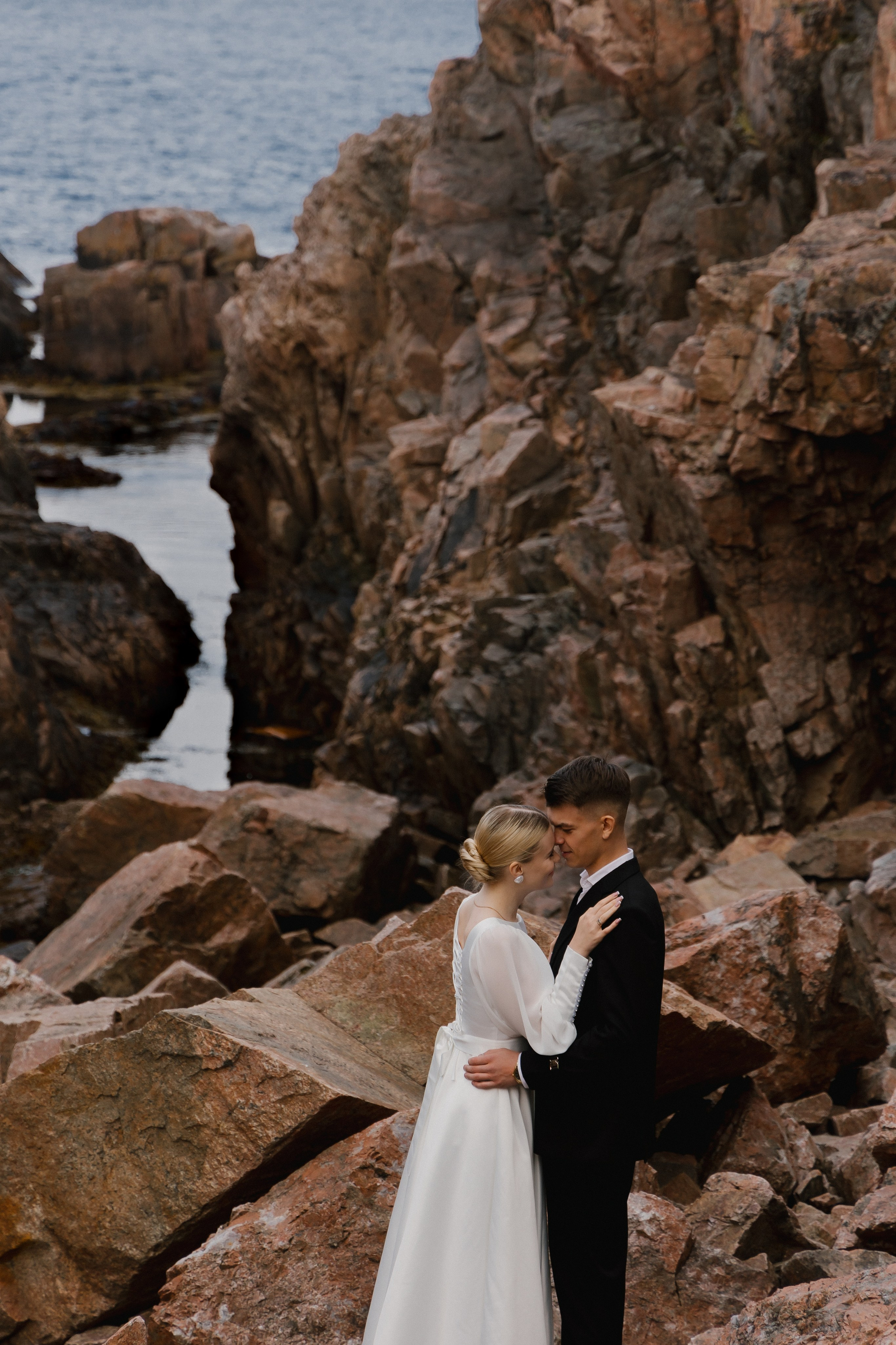 Шепот любви: молодые разговаривают тихо, сидя рядышком на влажных камнях у воды.