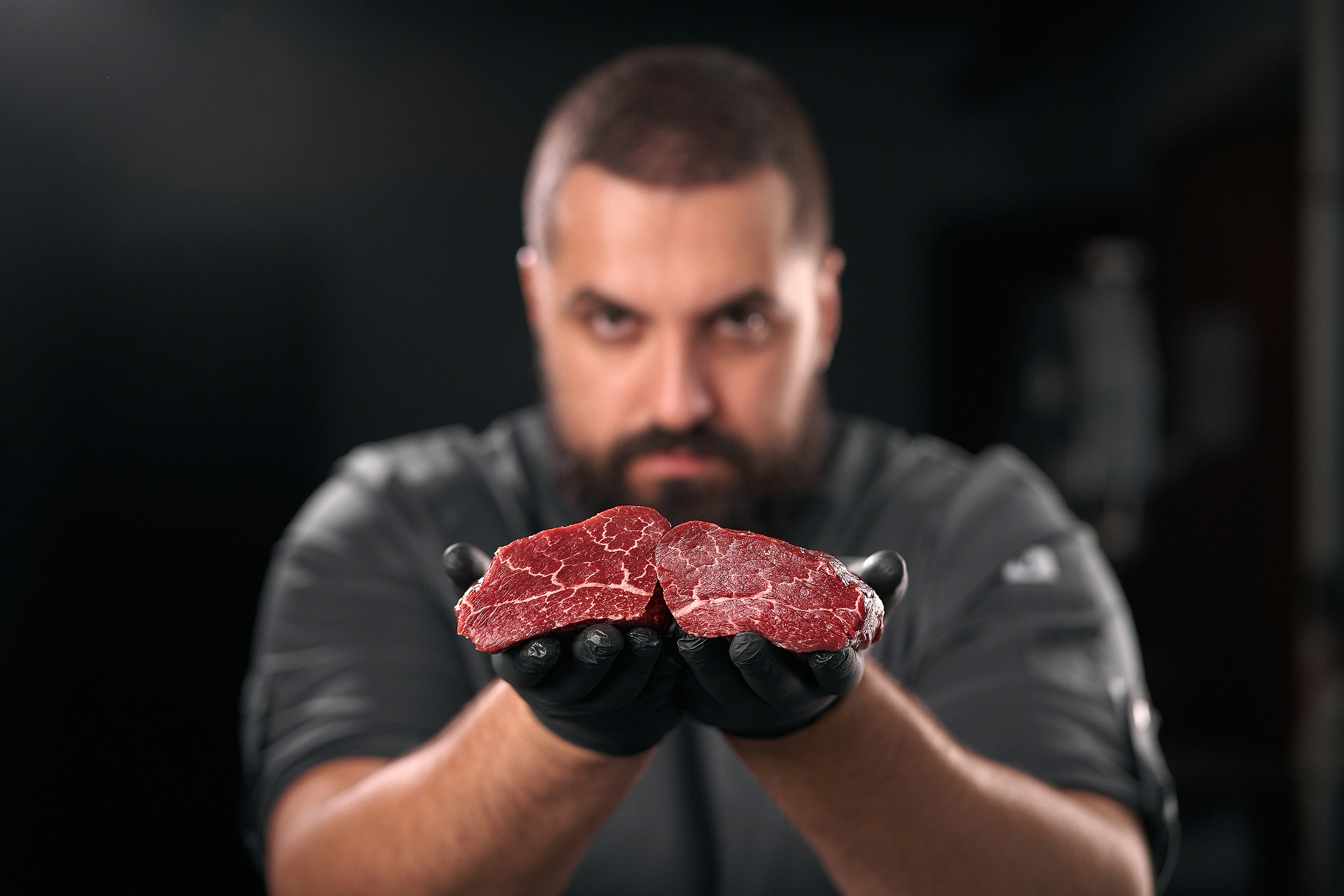 Мясник держит говяжью вырезку в руках на черном фоне