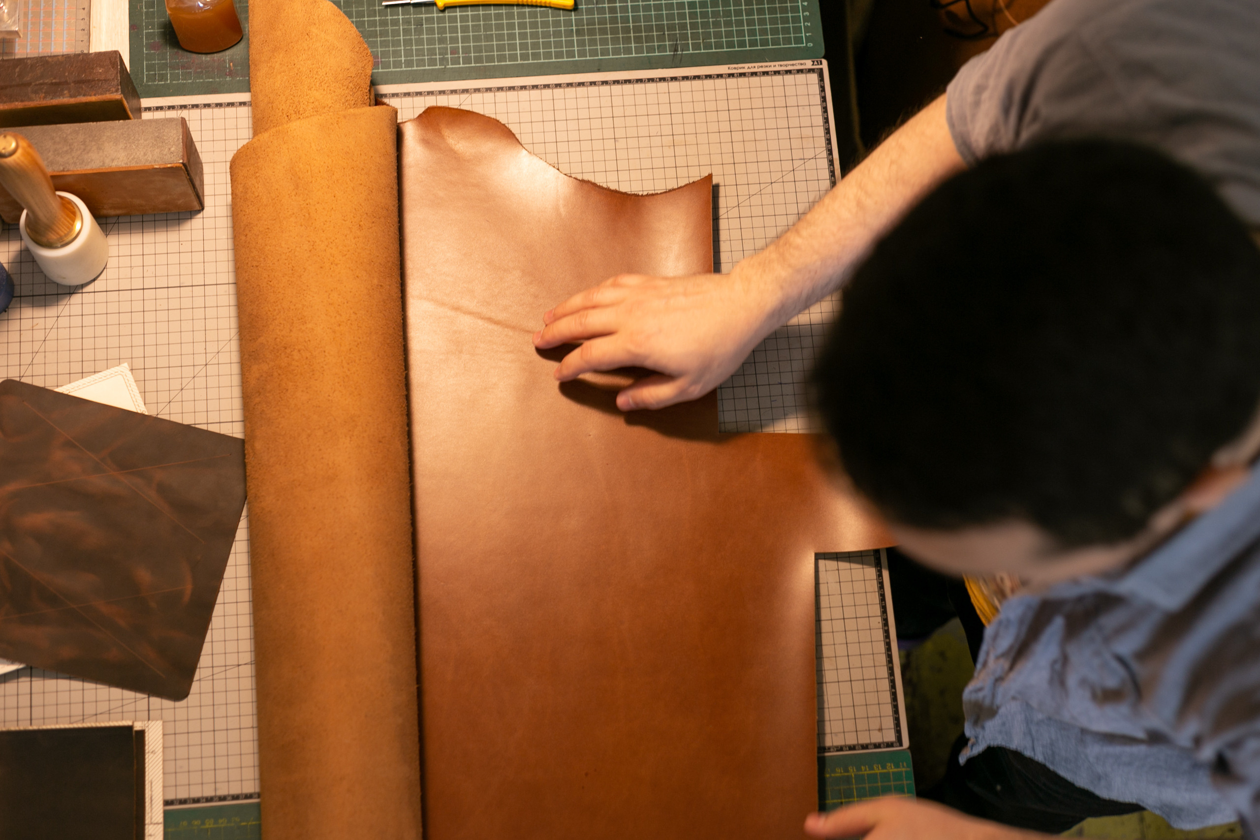 Вид сверху, мастер кожевенник развернул на столе коричневую кожу. Мягкий теплый свет.