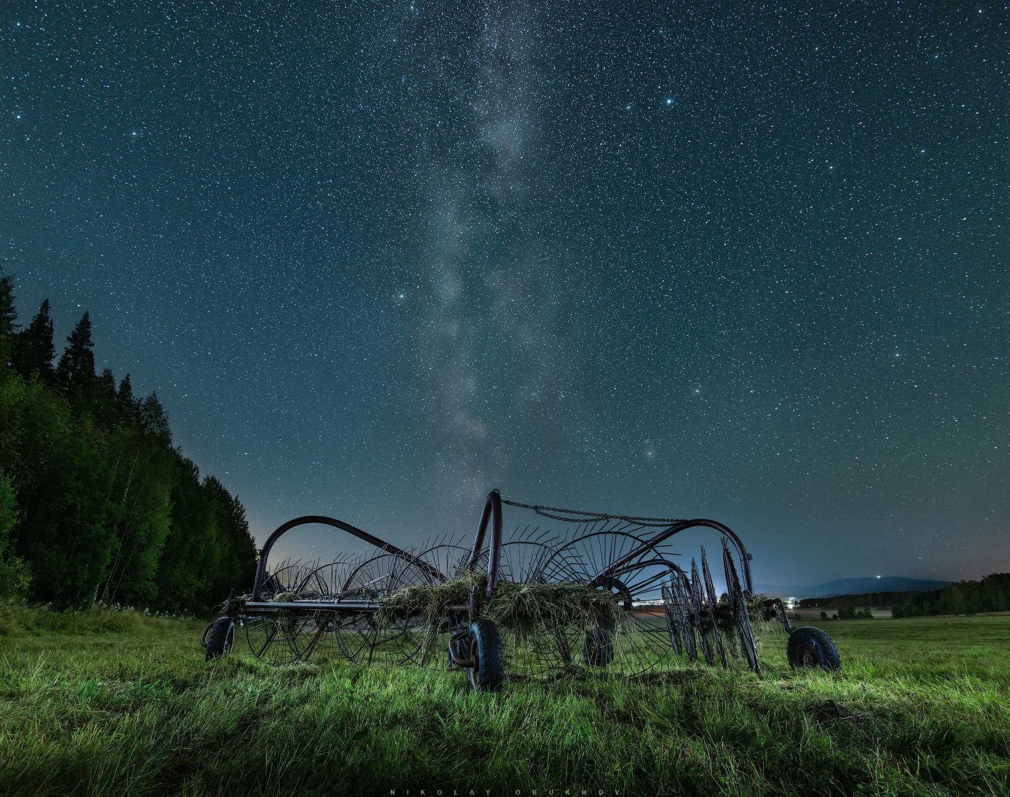 Сельский ночной пейзаж: на краю поля стоит стоит сельскохозяйственная техника под звездным небом.