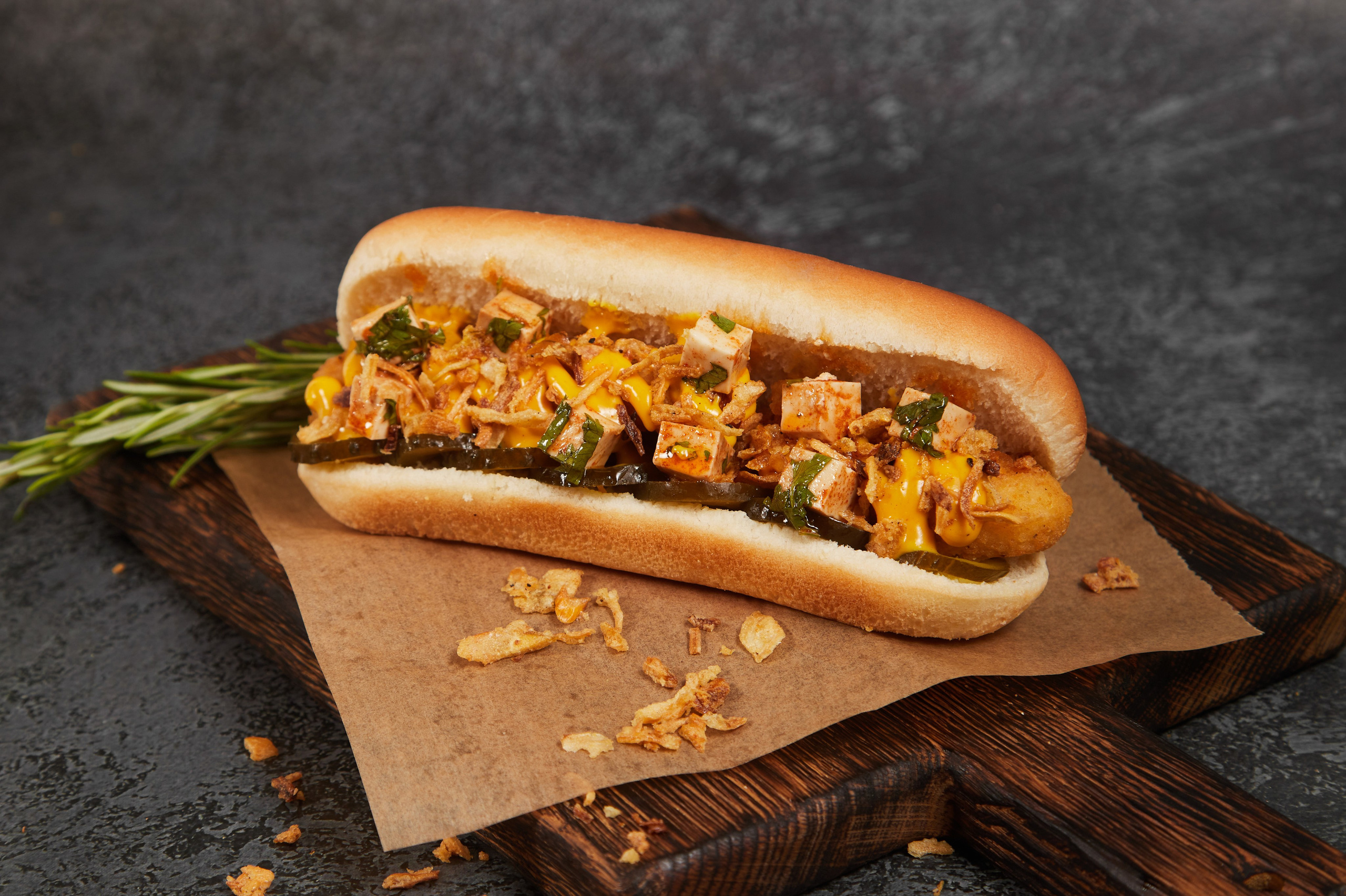 Хот-дог с овощами и мясной начинкой на деревянной доске.