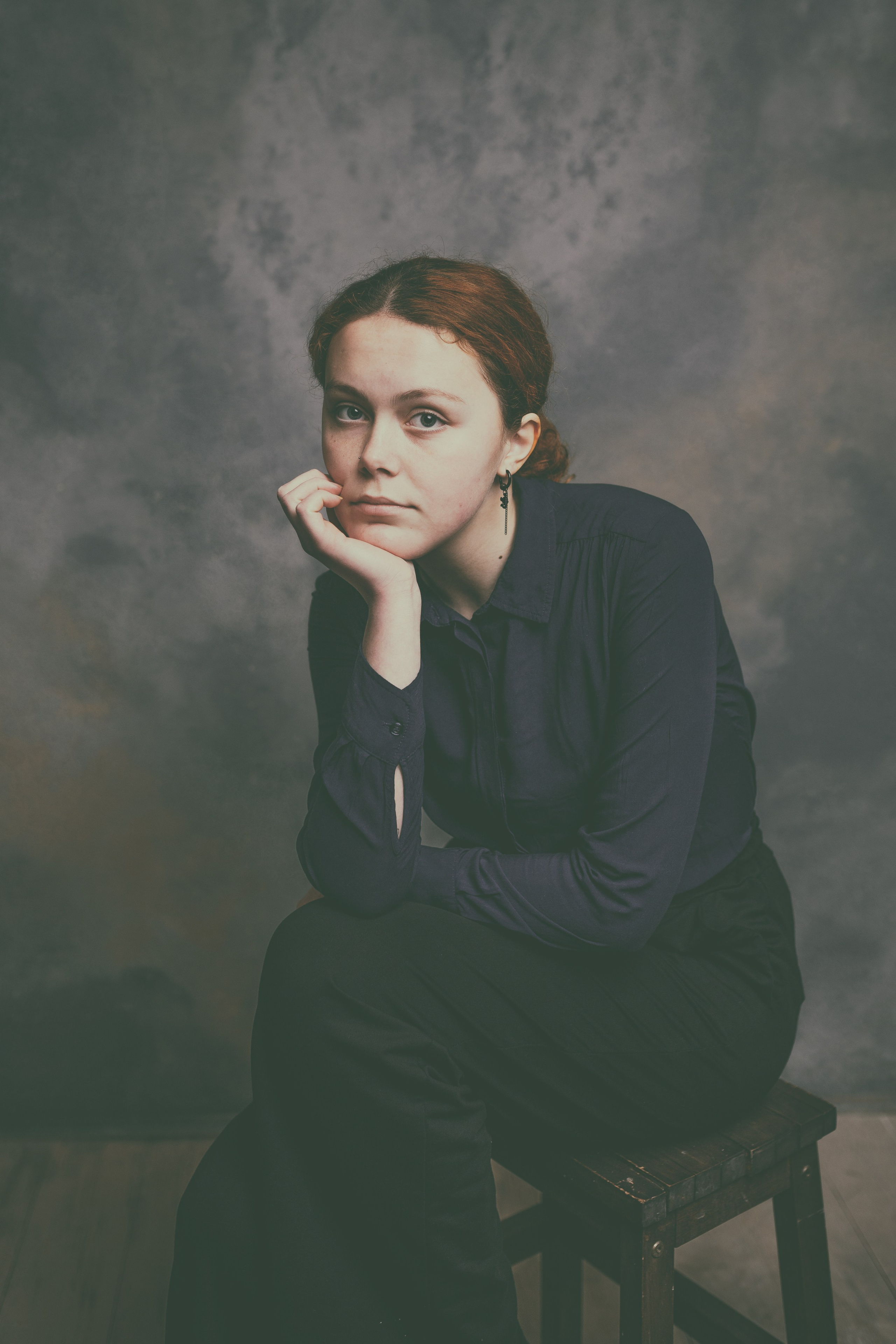 Модель в костюме сидит на стуле, подперев рукой подбородок