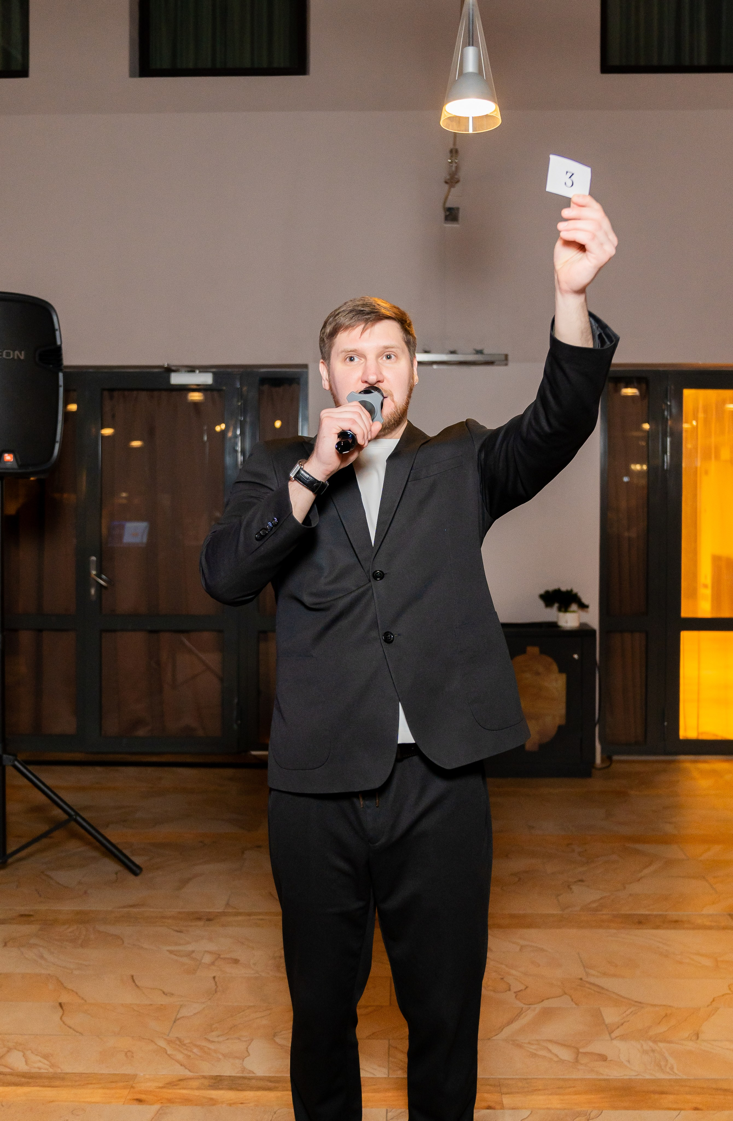 Ведущий с микрофоном высоко поднимает карточку с номером 3 и объявляет победителя розыгрыша в Radisson Sonya. Фото Евгения Мальцева (evrednix.ru).