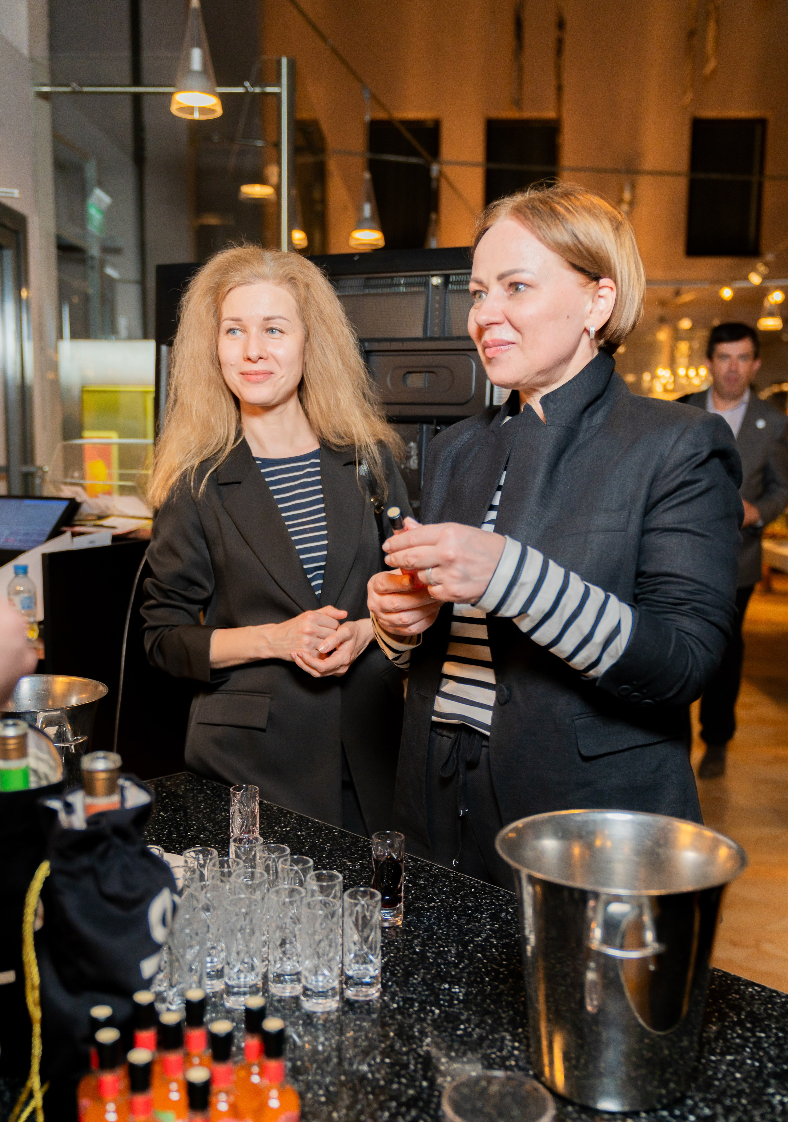 Две девушки у барной стойки на вечере в Radisson Sonya. Одна держит бутылочку. Фото Евгения Мальцева (evrednix.ru).