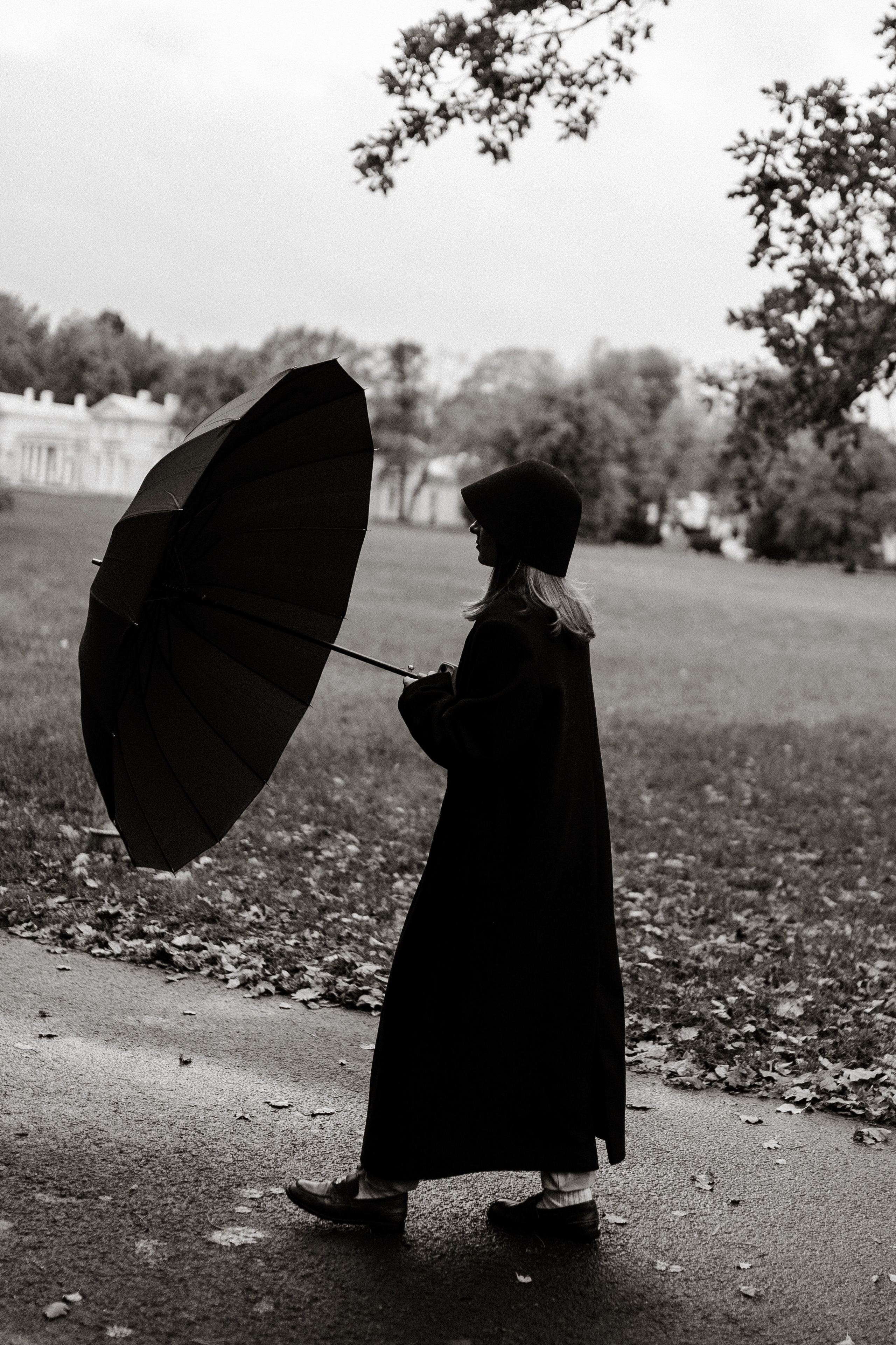 Чёрно-белый снимок девушки с раскрытым зонтом и в длинном пальто гуляющей по осеннему парку Санкт-Петербурга ЦКПиО им. Кирова 