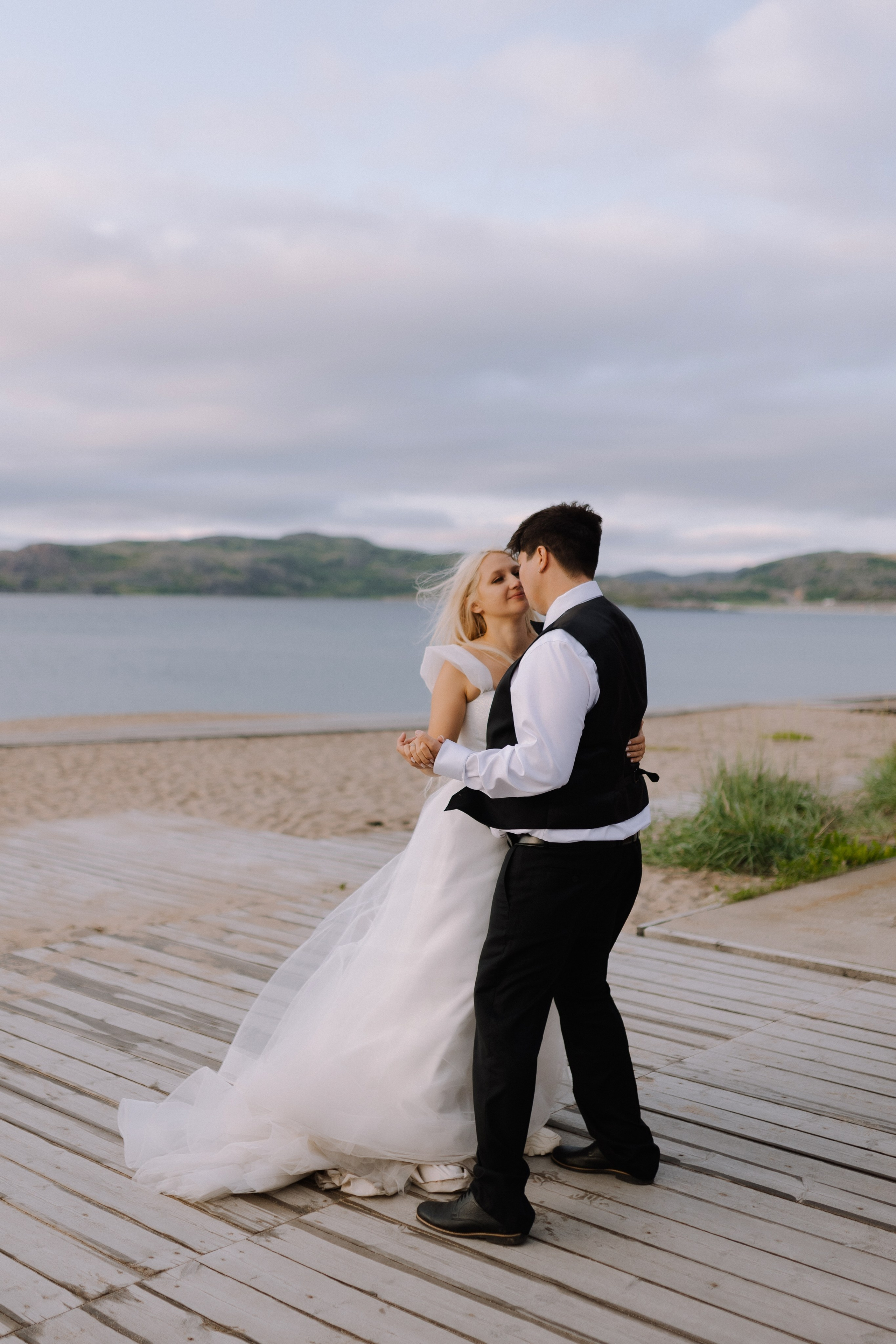 Закат солнца над Баренцевым морем и молодожёны, идущие рука об руку вдоль берега.