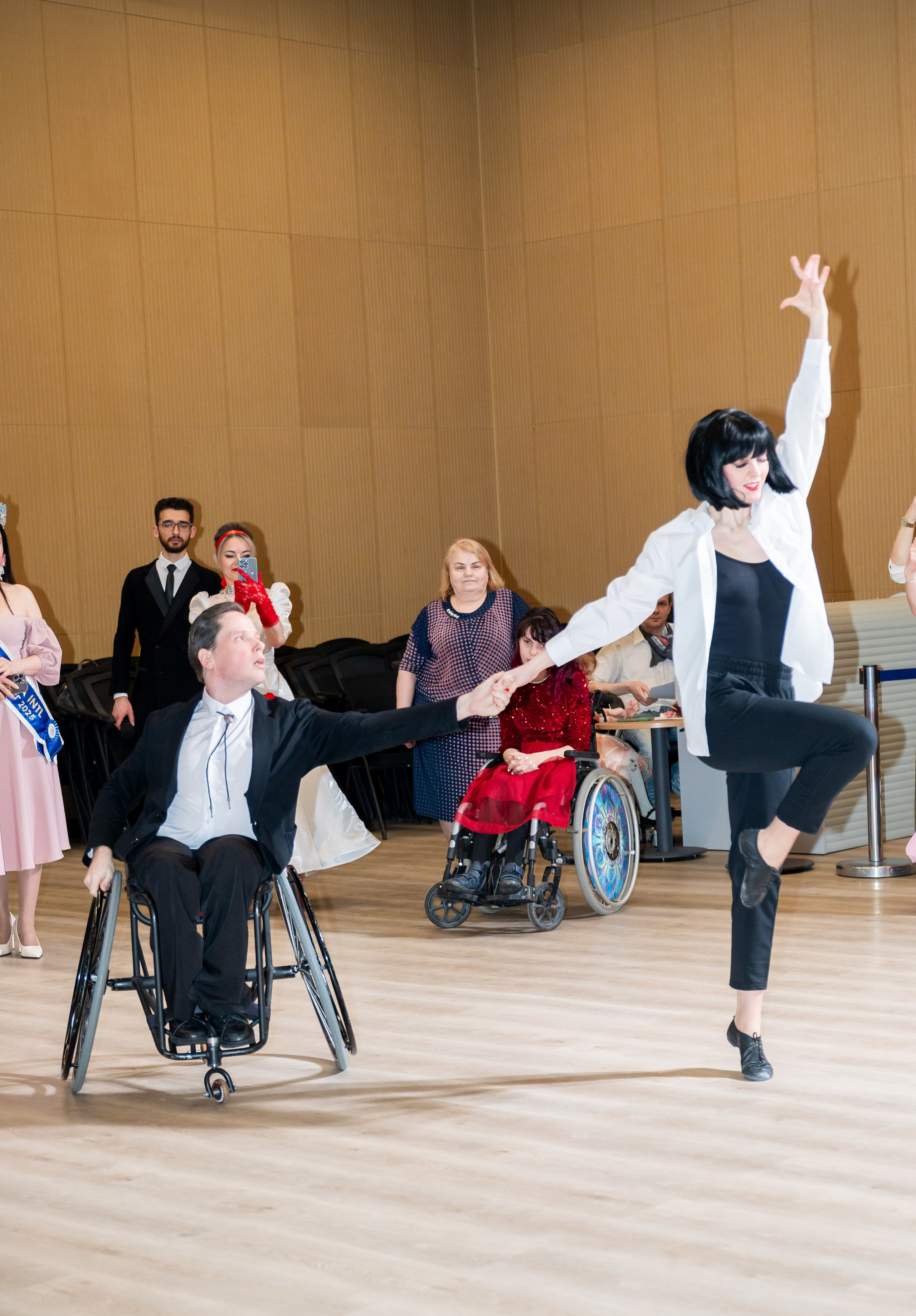 Танцевальная пара: девушка в белой рубашке и чёрном трико танцует с мужчиной в инвалидной коляске на инклюзивном балу. Фотограф Мальцев Евгений.