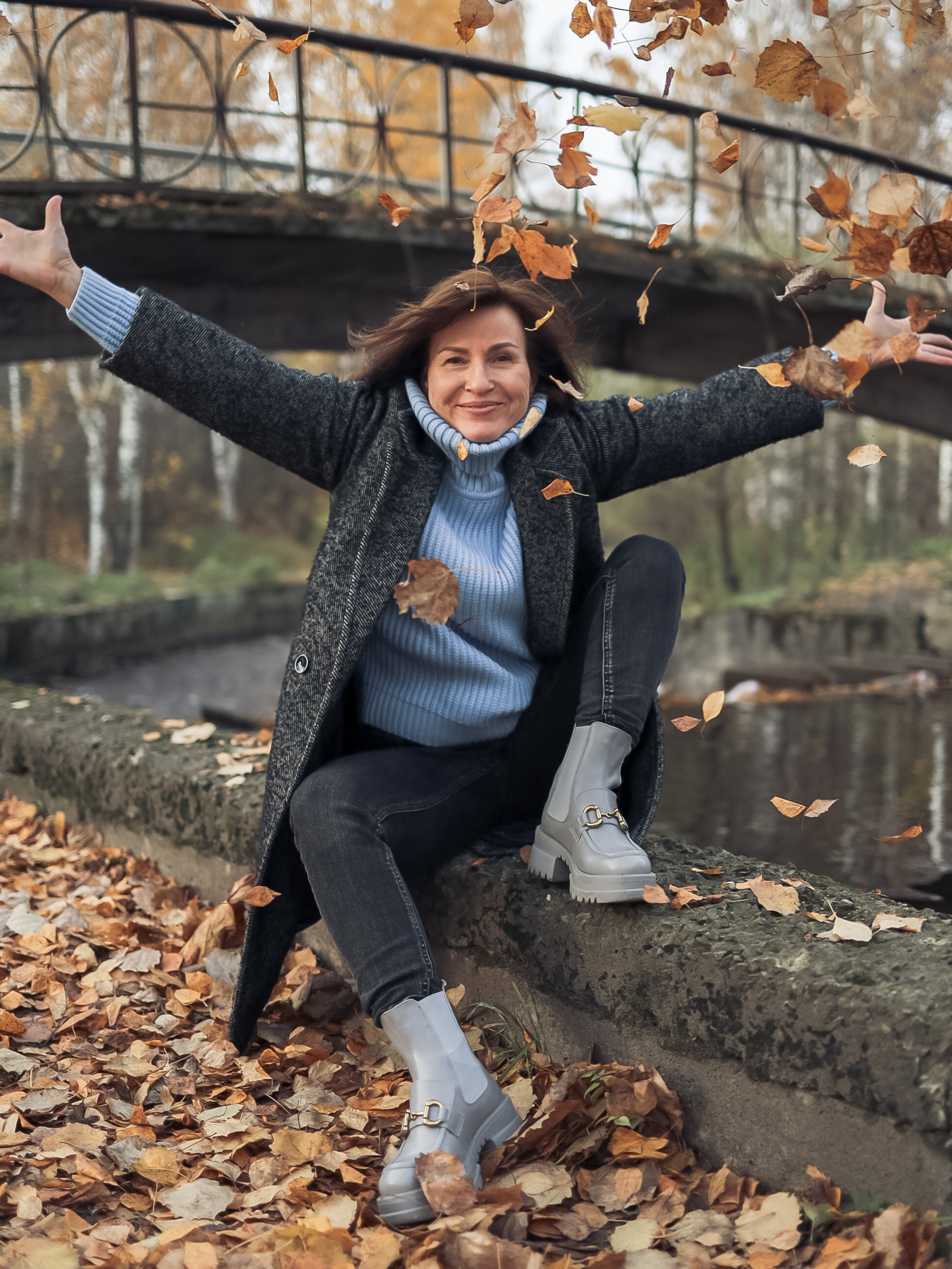 девушка сидит у реки и подбрасывает осенние листья 