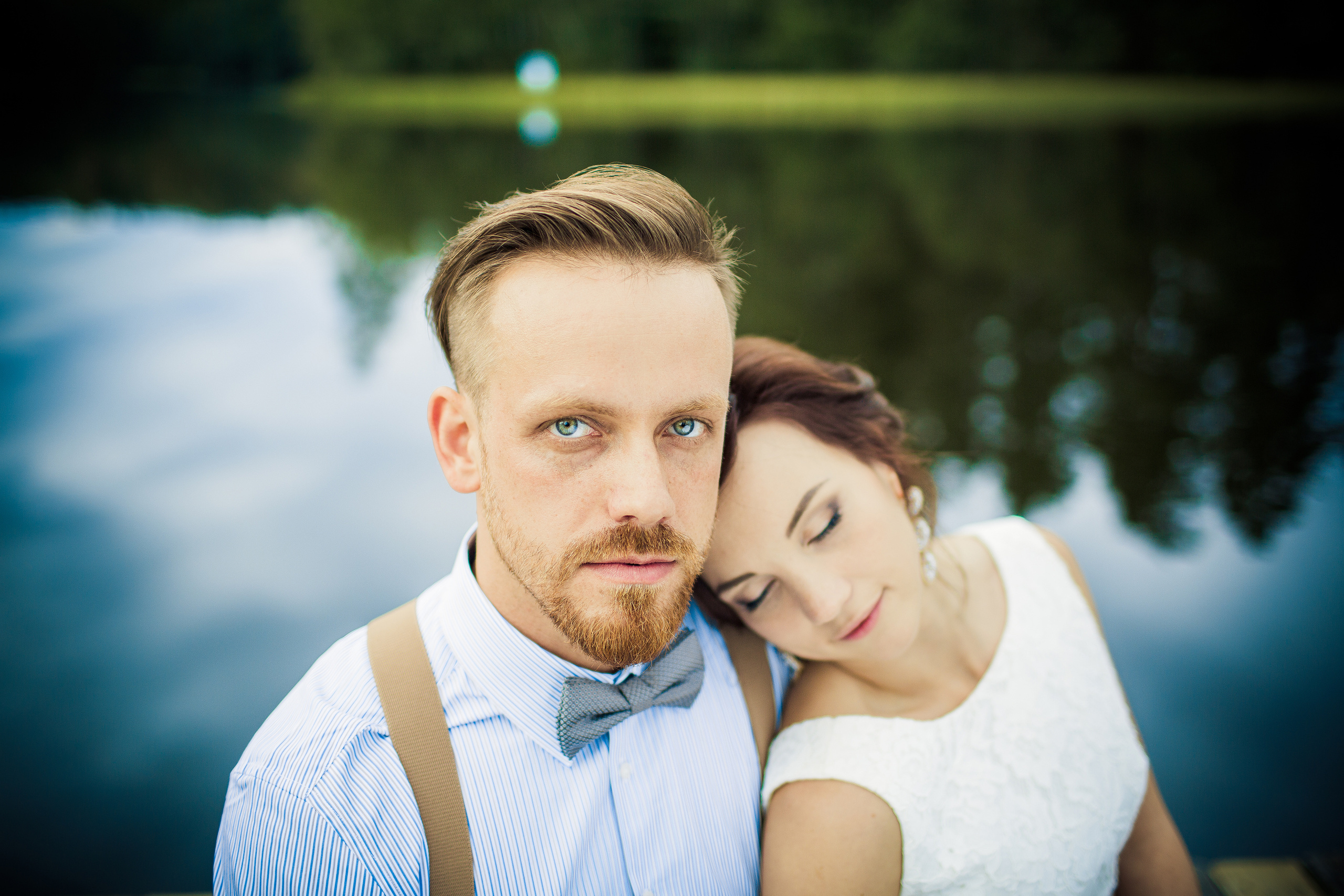 невеста прислонилась к зеленоглазому жениху на фоне воды и зелени