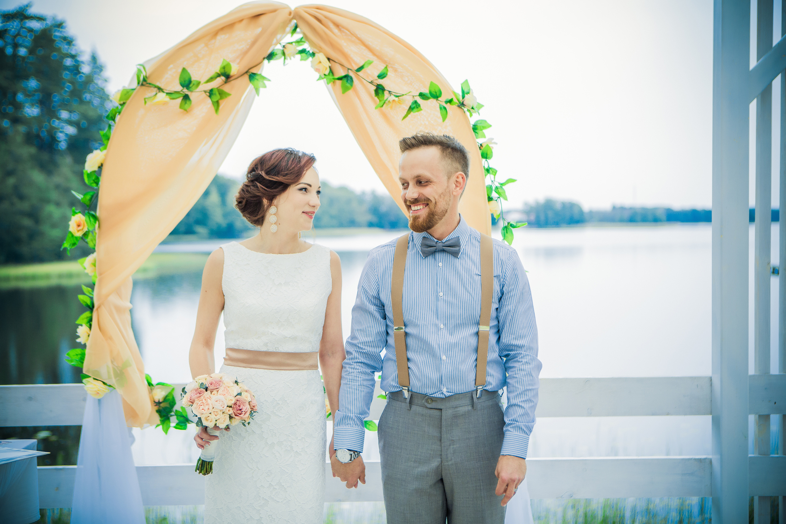 жених и невеста под свадебной аркой на берегу озера