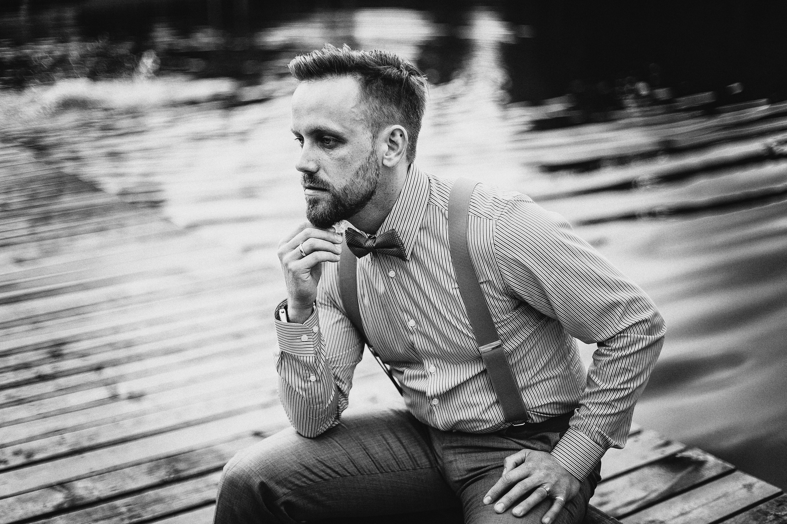 задумчивый стильный жених в подтяжках на деревянном причале